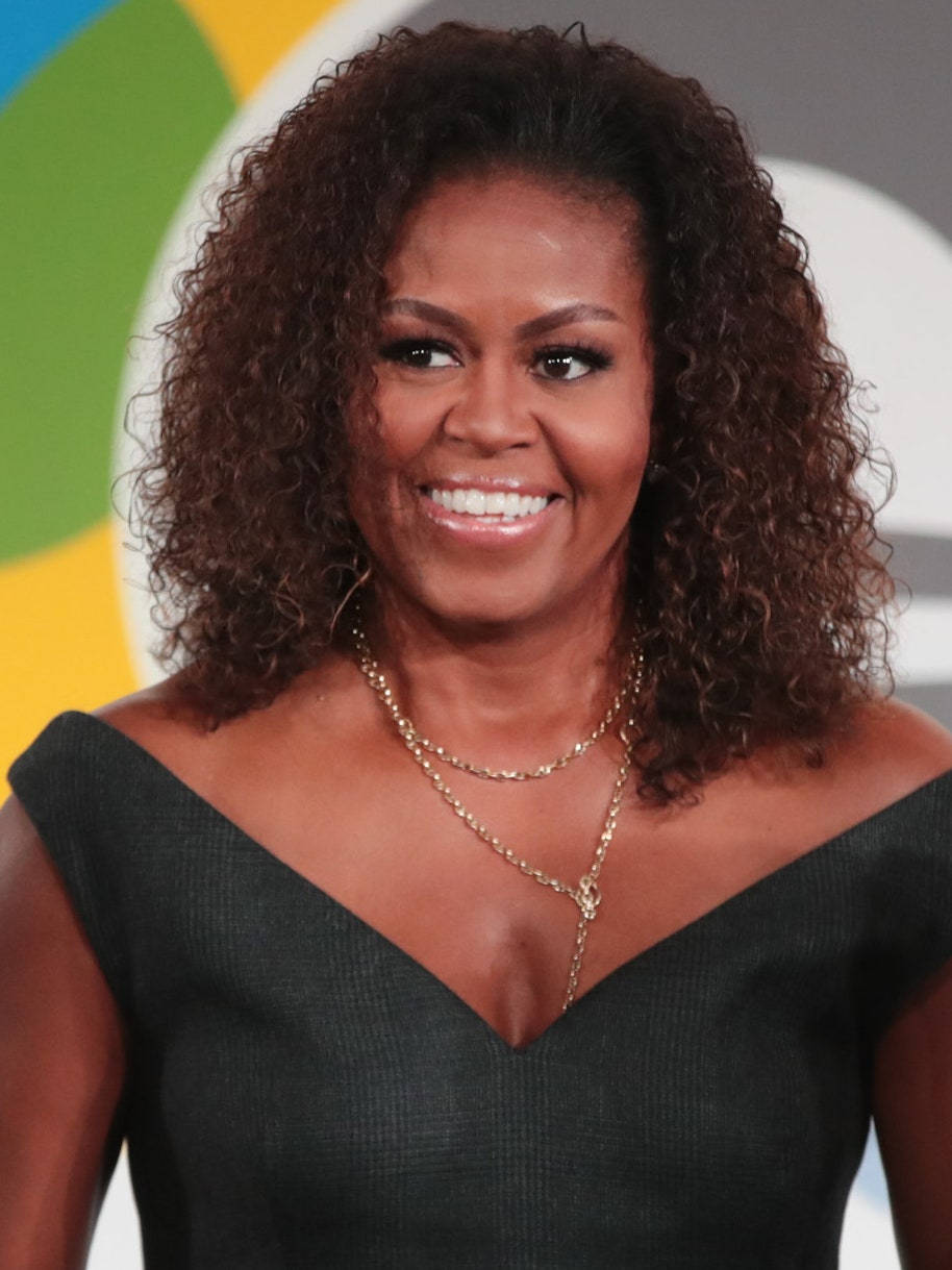 Michelle 桌布 壁紙 — 蜜雪兒·歐巴馬身穿黑色露肩連衣裙，搭配捲髮和金色層疊項鍊，溫暖微笑。