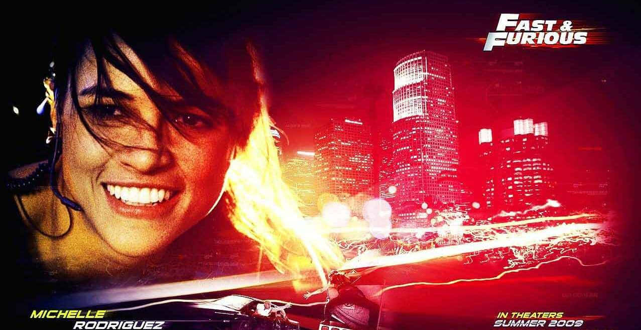 Fast And Furious 桌布 壁紙 — 蜜雪兒·羅德里奎茲在霓虹燈浸染的夜晚城市天際線背景下，一輛疾駛的汽車爆出火焰，她露出兇猛的笑容。