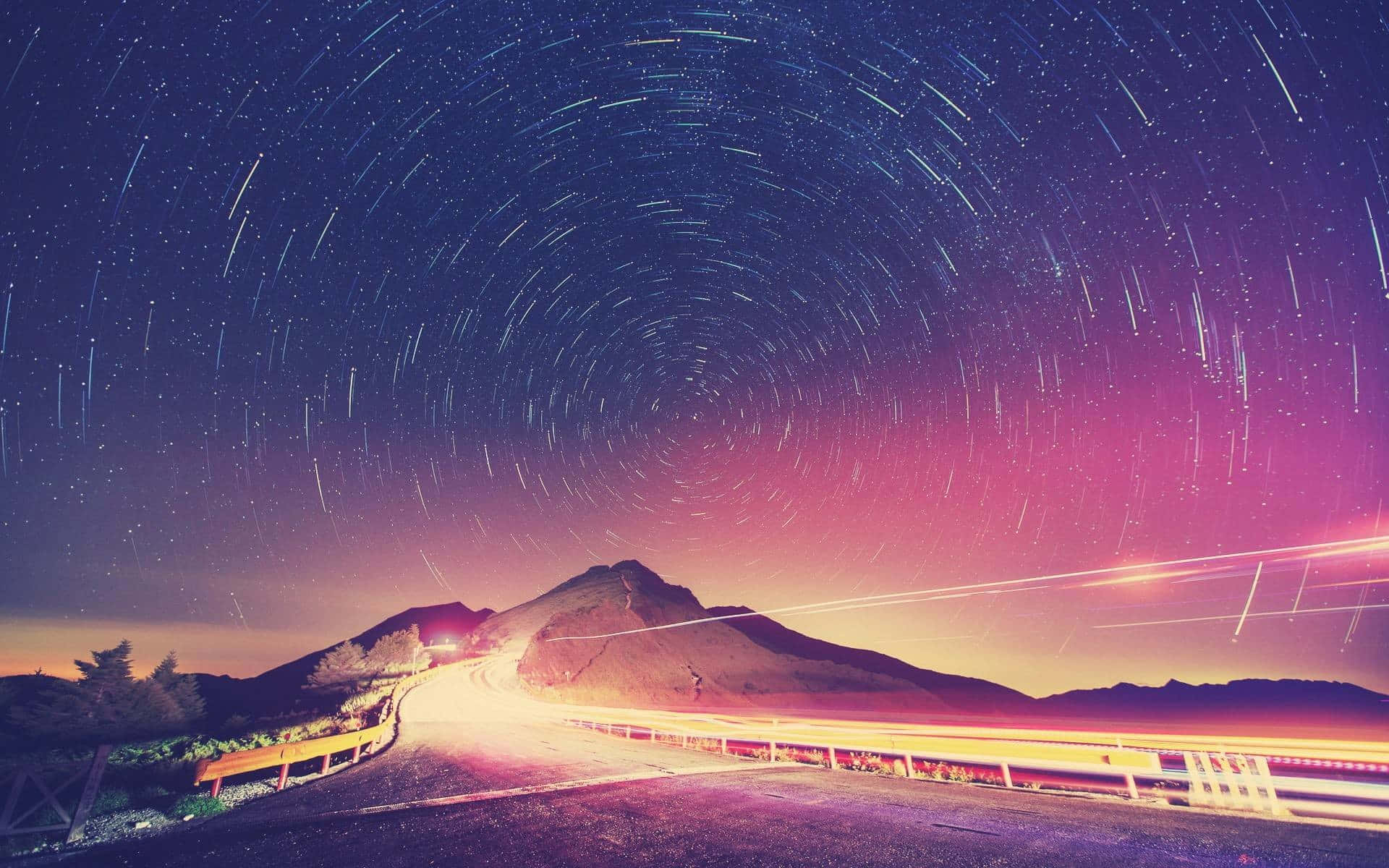 風景 桌布 壁紙 — 蜿蜒的山路，在充滿活力的夜空下，有旋轉的星軌和過往車輛發出的發光光條。