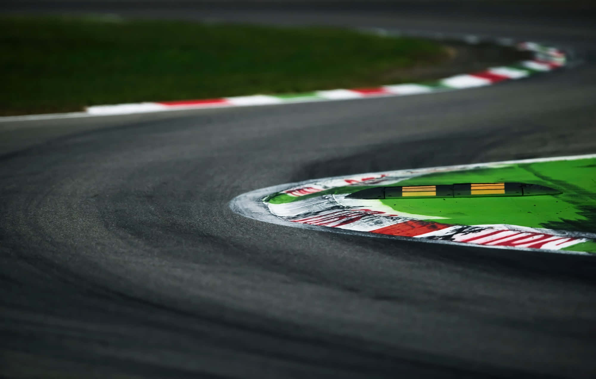 Race Track 桌布 壁紙 — 蜿蜒的瀝青賽道彎角特寫，邊緣有紅、白、綠色路緣石，遠處有草地。