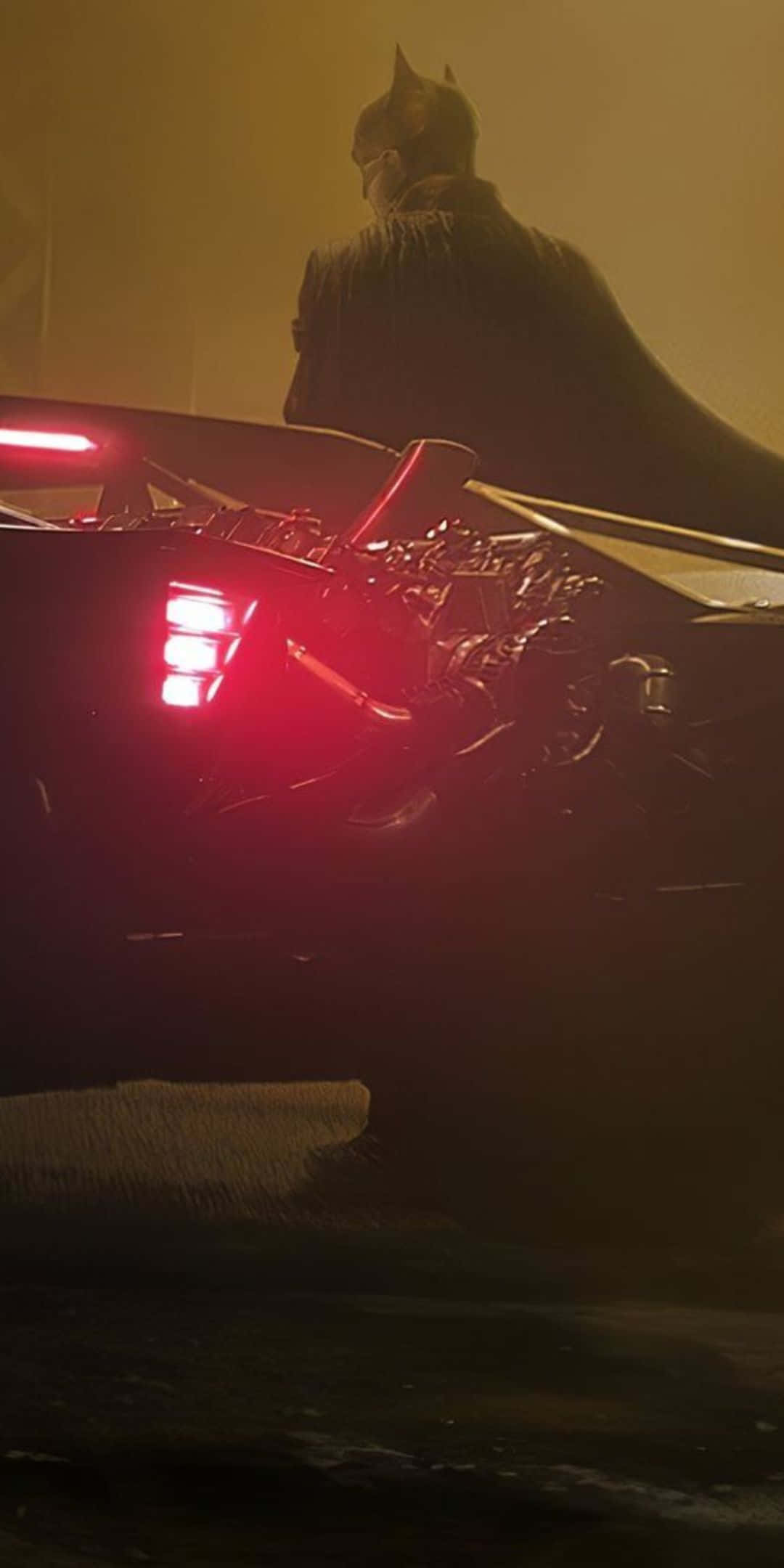 Pixel 3 Batmobile 桌布 壁紙 — 蝙蝠俠以剪影姿態站在其裝甲蝙蝠車後方，蝙蝠車在煙霧瀰漫的夜晚場景中發出紅光。