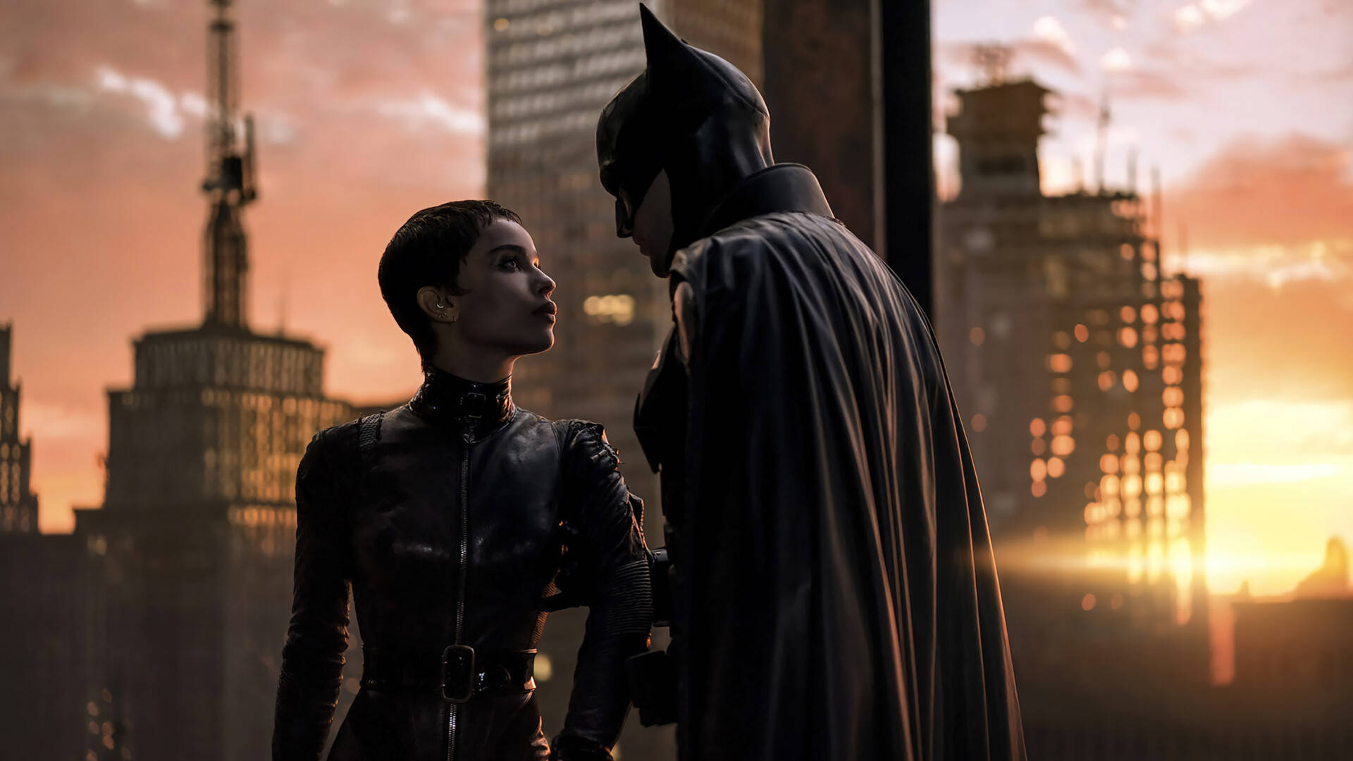 Catwoman 桌布 壁紙 — 蝙蝠俠和貓女在屋頂上面對面站立，夕陽落在城市天際線後方。