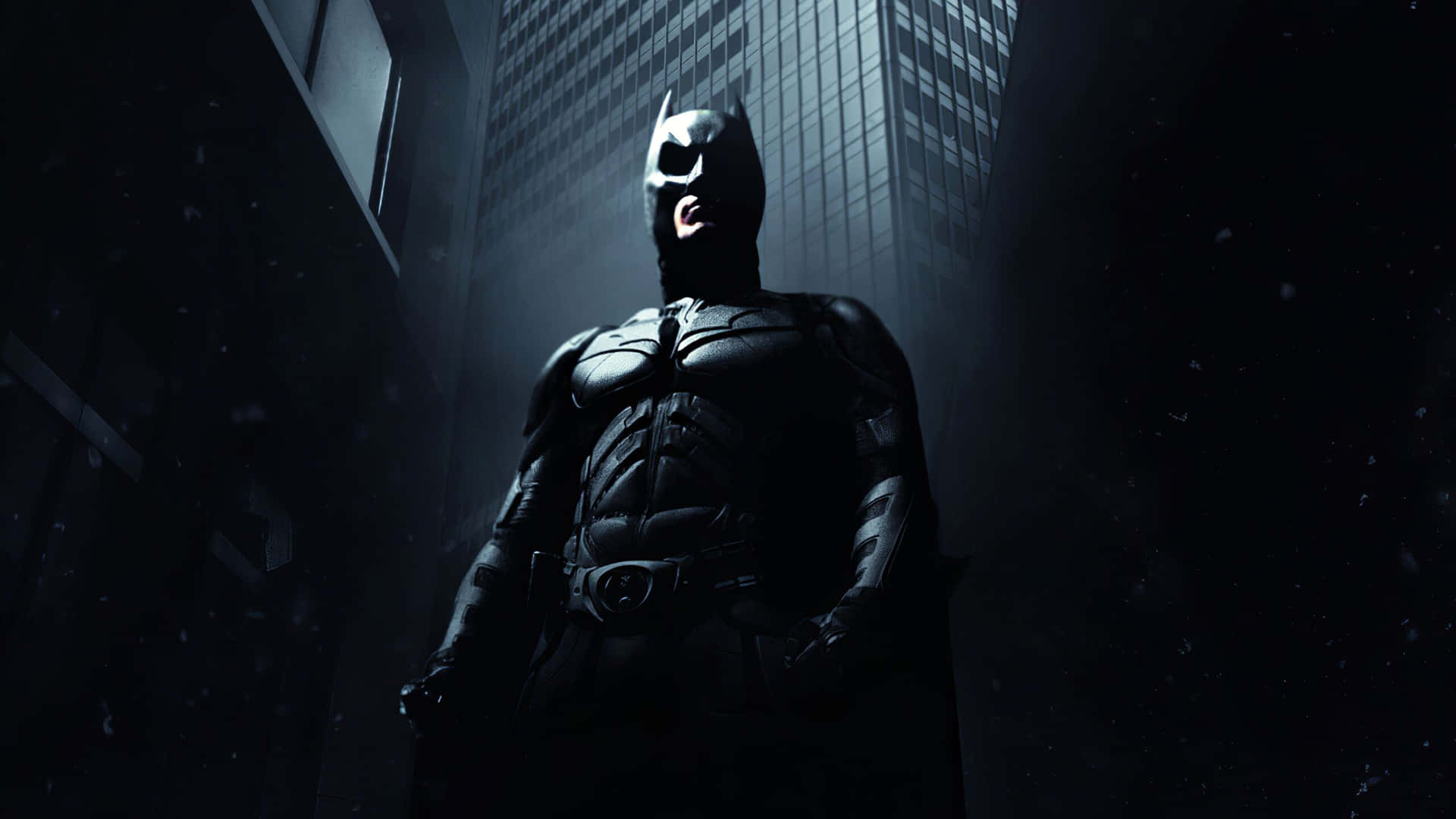 Batman Desktop 桌布 壁紙 — 蝙蝠俠在戲劇性的背光下，高聳地站在高聳摩天大樓之間一條黑暗、被雨水浸透的小巷中。