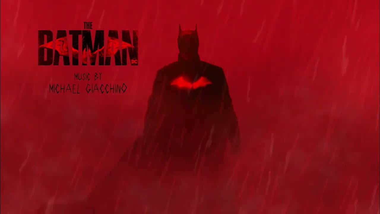 Batman Year One 桌布 壁紙 — 蝙蝠俠在暴風雨的紅色暴雨中呈現剪影，發光的蝙蝠標誌、電影標題和作曲家鳴謝清晰可見。