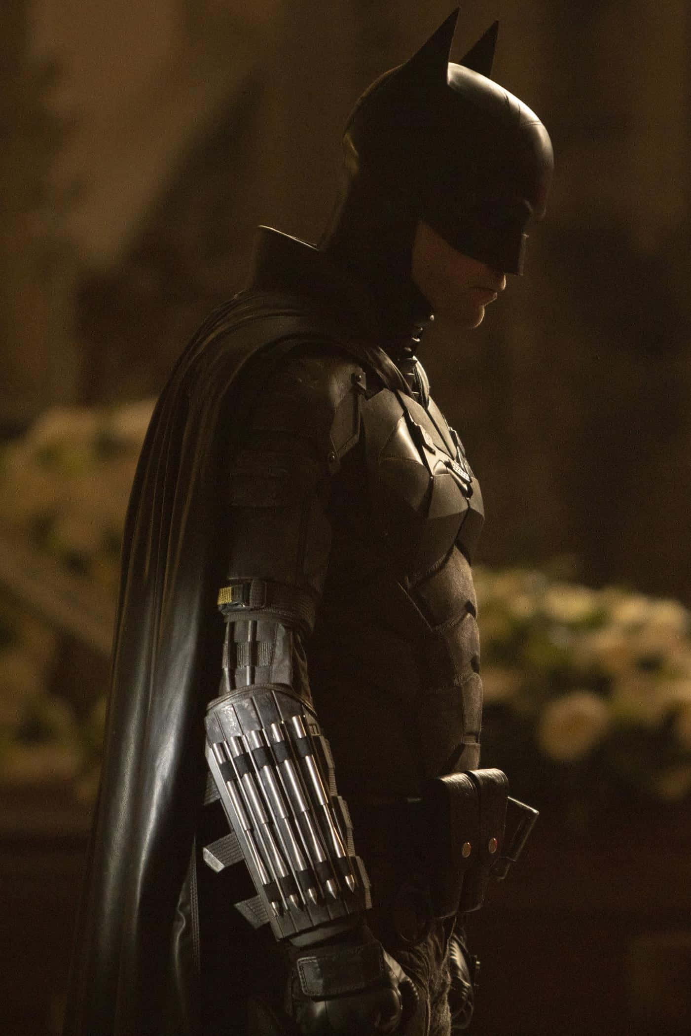 Bat-suit 桌布 壁紙 — 蝙蝠俠在溫暖的環境光線下，身穿裝甲服和披風，以陰影側面站立。