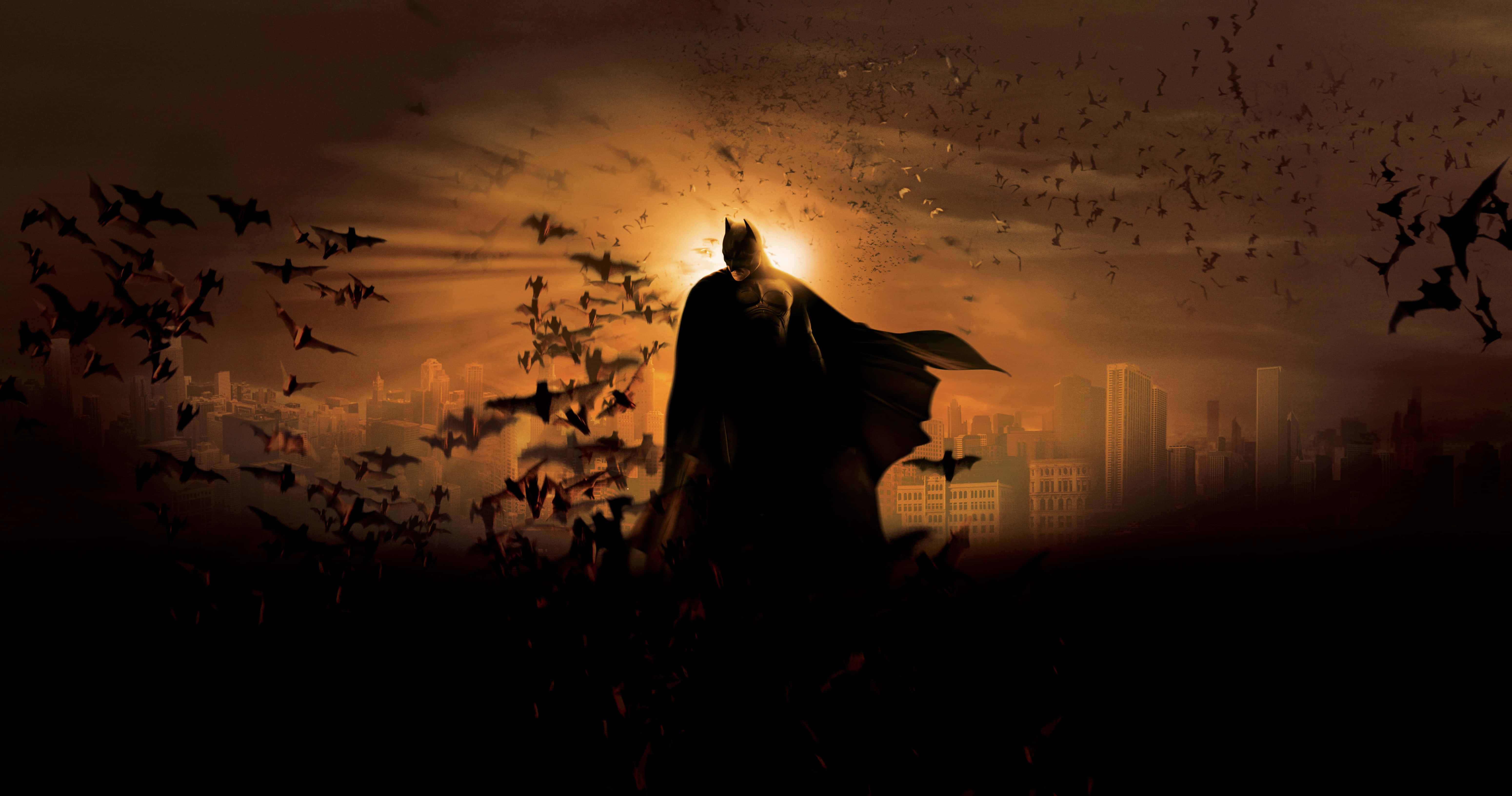 Gotham City 桌布 壁紙 — 蝙蝠俠在發光的日落中呈現剪影，蝙蝠在他周圍的城市天際線上成群飛舞。