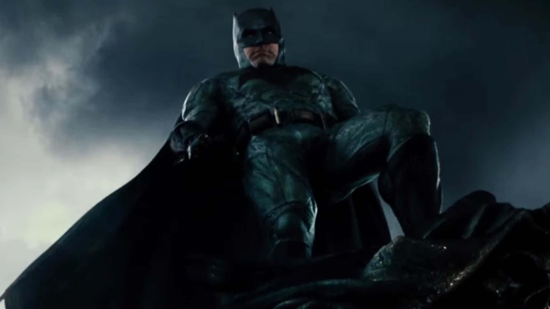 Zack Snyders Justice League 桌布 壁紙 — 蝙蝠俠坐在黑暗廢墟頂端，暴風雨的天空下，他的斗篷隨風飄揚，身後閃電閃爍。