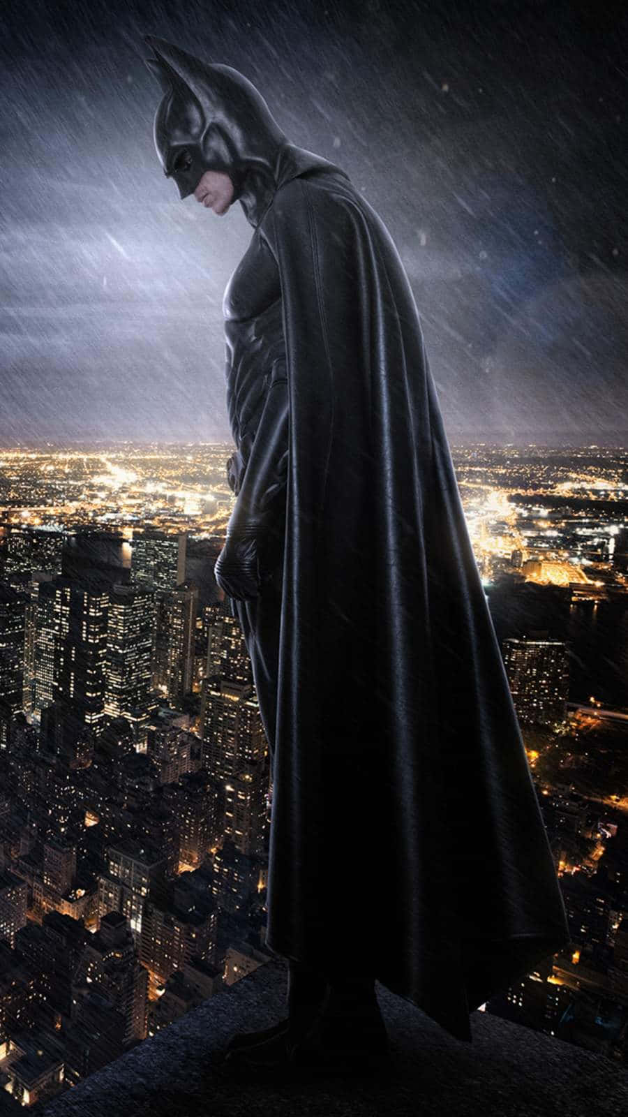 Batman City 桌布 壁紙 — 蝙蝠俠獨自站在屋頂上，俯瞰夜晚被雨水浸濕的城市景觀，下方燈光閃爍。