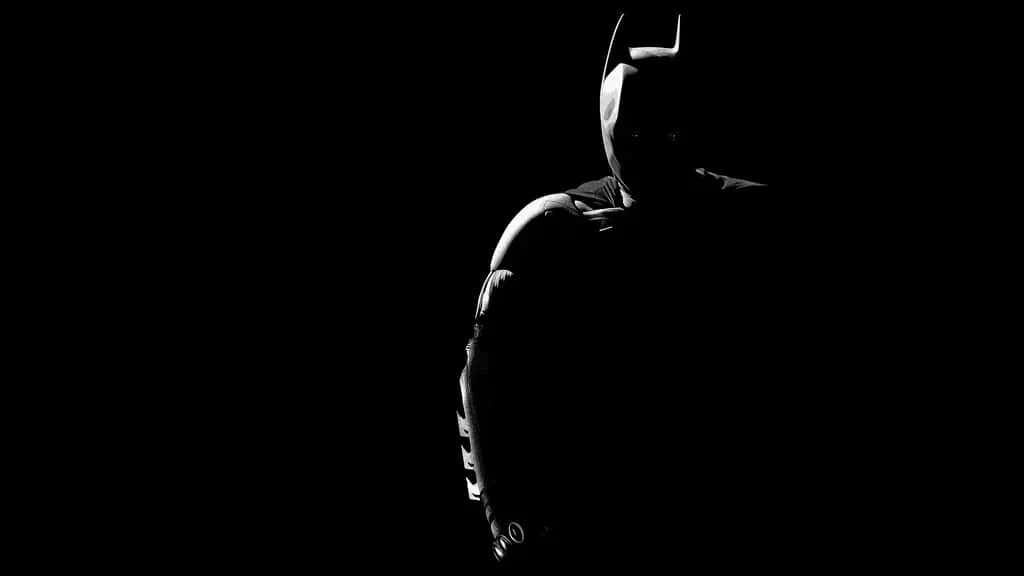 1920 X 1080 Batman 桌布 壁紙 — 蝙蝠俠的鮮明剪影矗立在近乎完全的黑暗中，只有微弱的高光勾勒出他的頭罩和裝甲服。