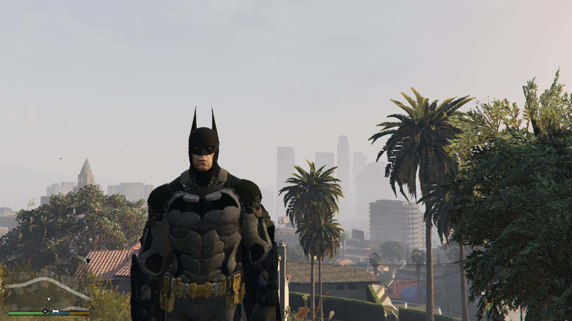 Bat-suit 桌布 壁紙 — 蝙蝠俠站在一個朦朧的城市景觀中，棕櫚樹和遠處的摩天大樓在蒼白的天空下。