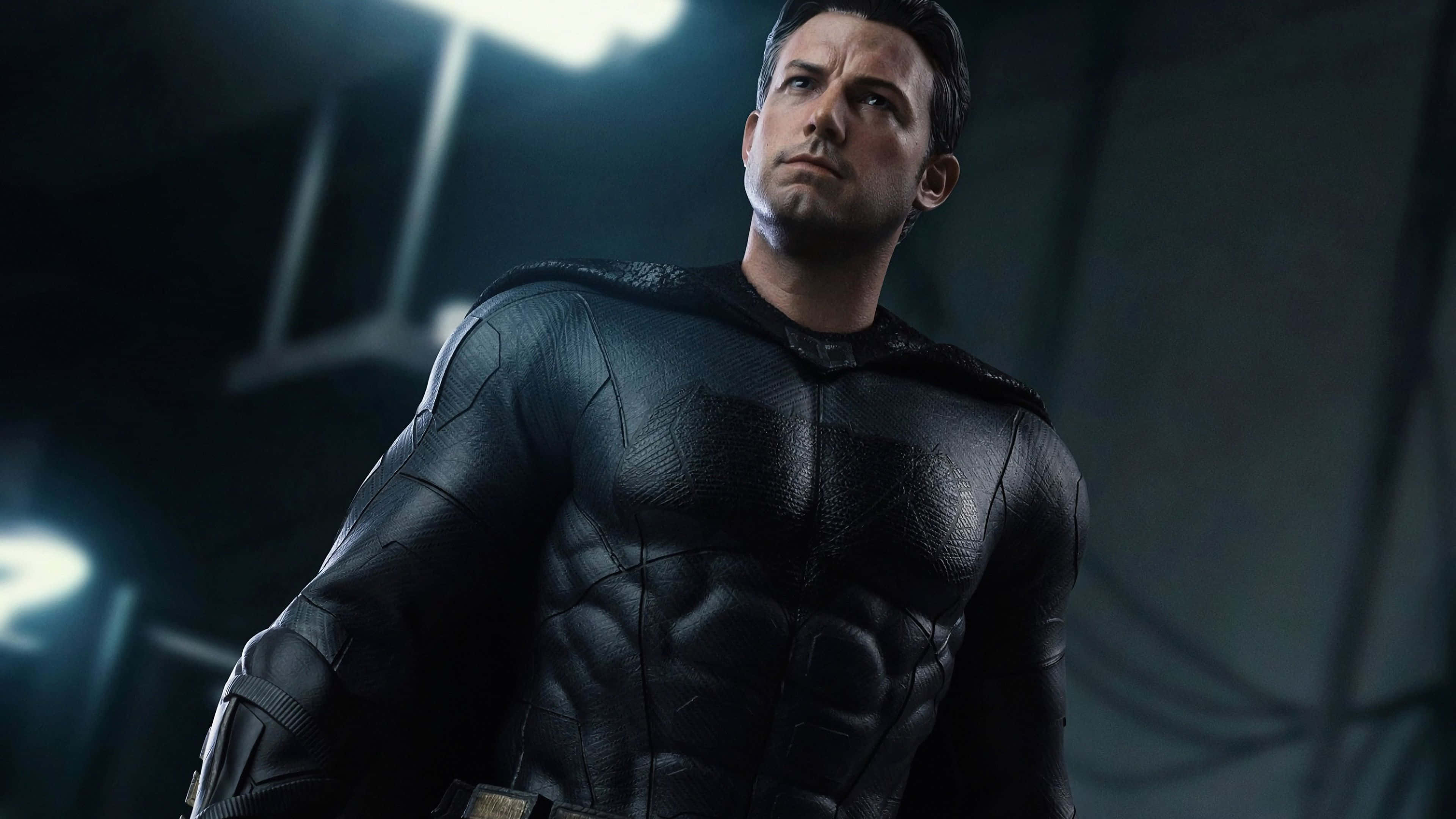 Ben Affleck 桌布 壁紙 — 蝙蝠俠站在光線昏暗的工業環境中，他的裝甲服在刺眼的頭頂燈光下閃閃發光。