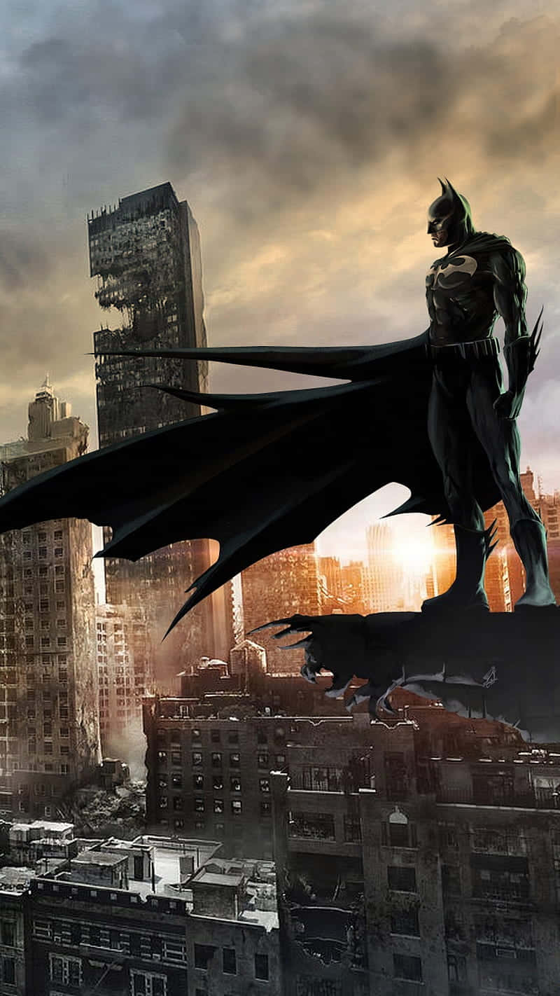 Batman City 桌布 壁紙 — 蝙蝠俠站在摩天大樓的屋頂上，背景是戲劇性的日落天空，下方有煙霧和受損的建築物。