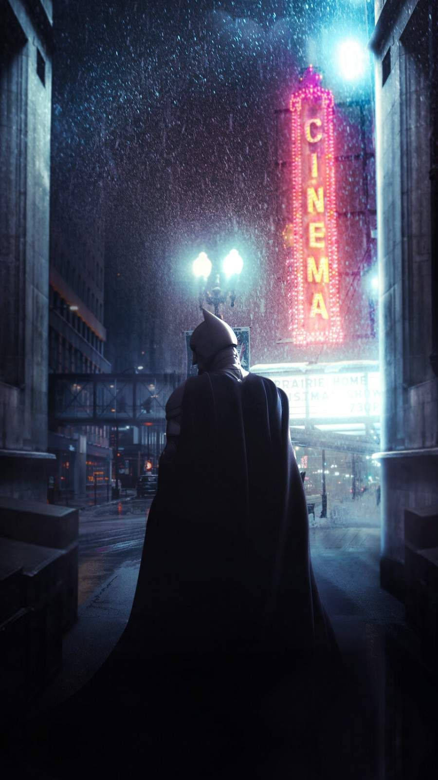The Batman iPhone 桌布 壁紙 — 蝙蝠俠站在被雨水浸濕的高譚市小巷中，凝視著街燈下閃爍的紅色電影院招牌。