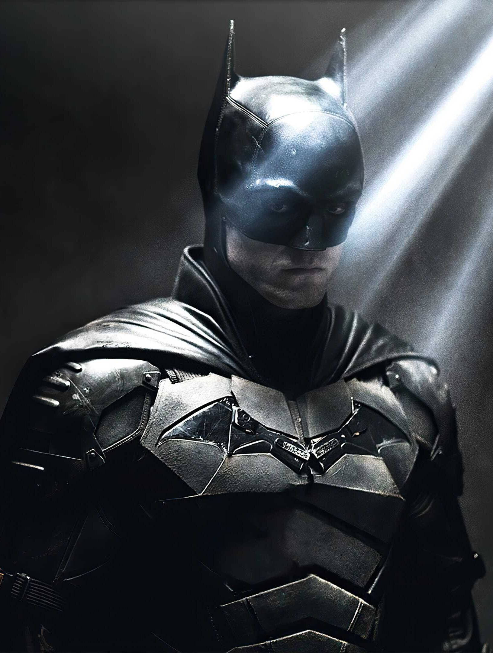 The Batman iPhone 桌布 壁紙 — 蝙蝠俠站在陰影中，戲劇性的光束穿過煙霧，突顯他的裝甲服和堅定的表情。