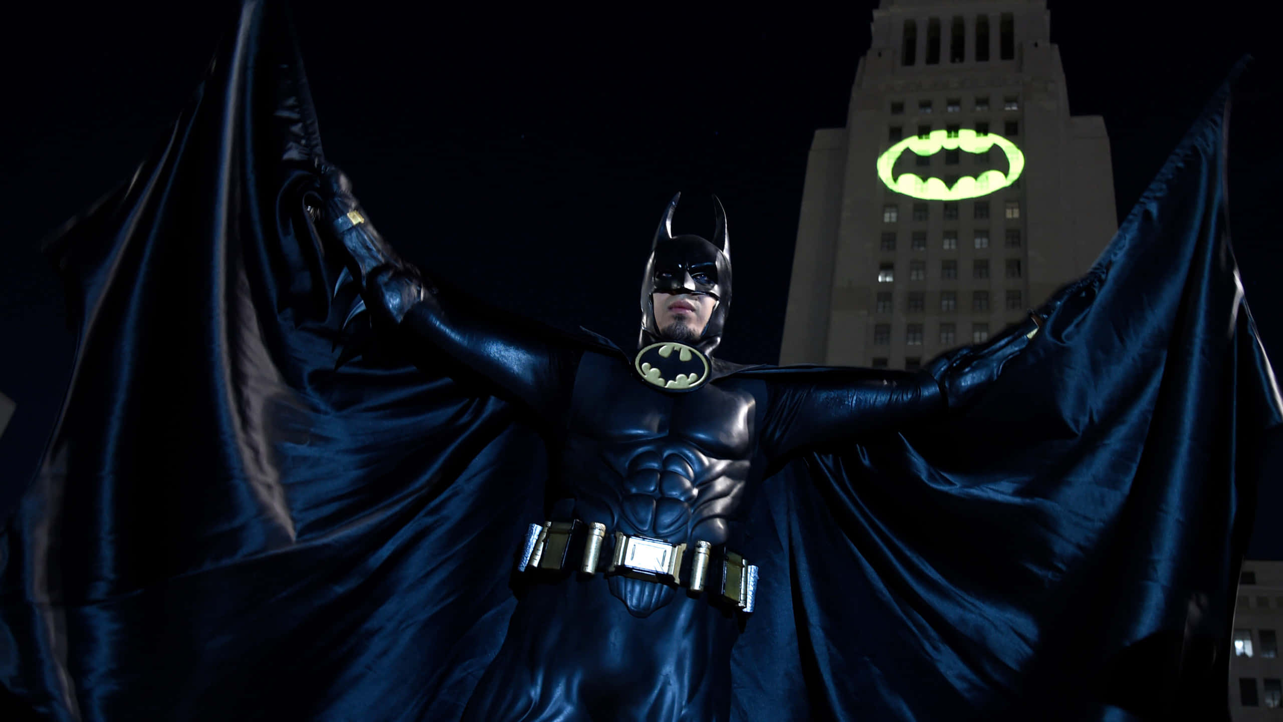 Bat Signal 桌布 壁紙 — 蝙蝠俠英雄式地站在黑暗的城市天際線前，斗篷張開，建築物上有一個發光的蝙蝠標誌。