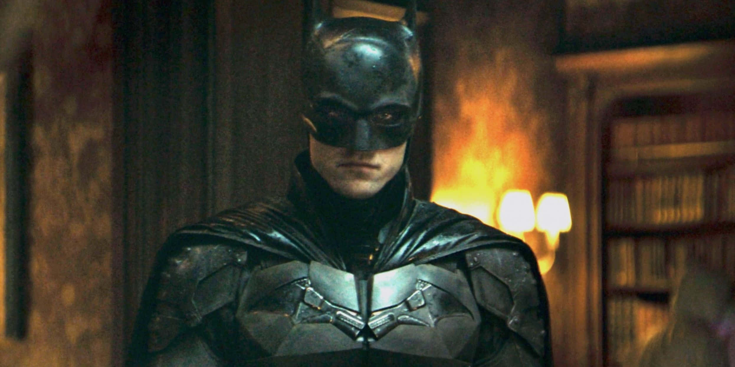 Bat-suit 桌布 壁紙 — 蝙蝠俠莊嚴地站在燈光昏暗的圖書館中，身後火焰爆發，投射出不祥的光芒。