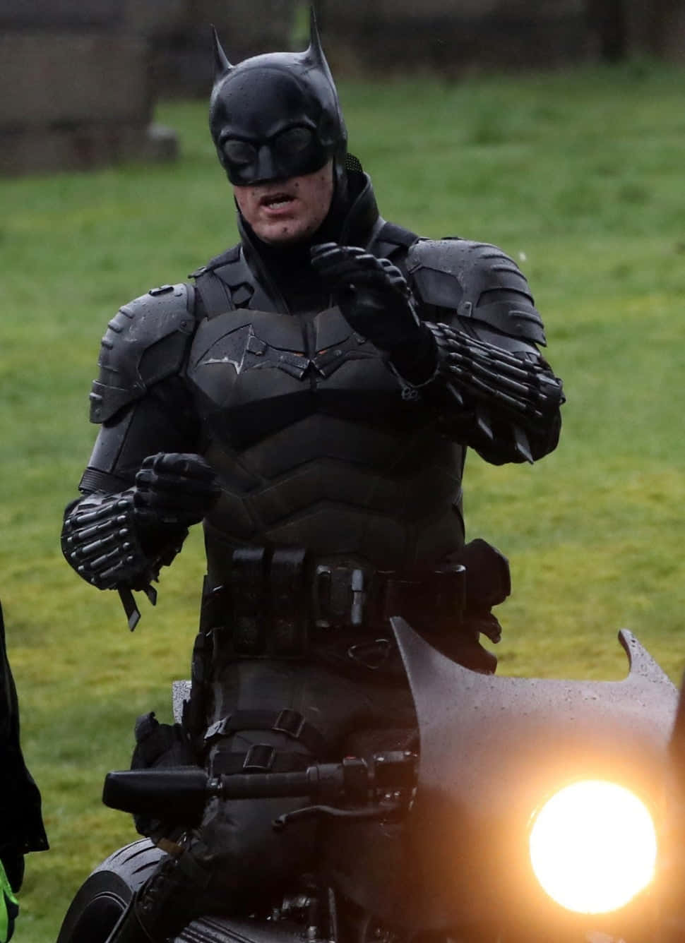 Bat-suit 桌布 壁紙 — 蝙蝠俠身穿全副盔甲，騎著一輛帶有發光頭燈的機車穿過草地。