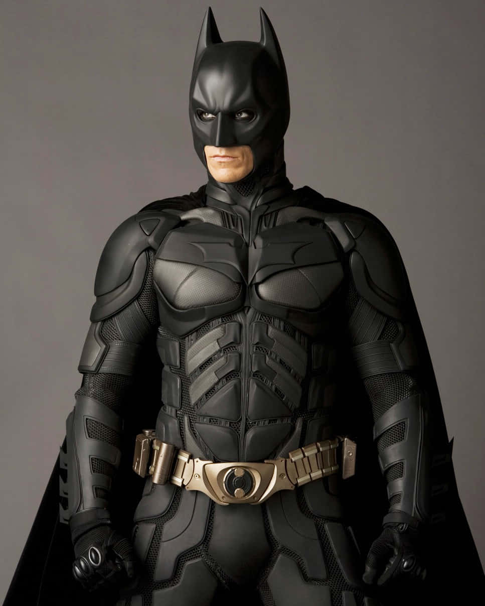 Bat-suit 桌布 壁紙 — 蝙蝠俠身穿黑色裝甲服配金色腰帶，站在灰色背景前的全身照片。