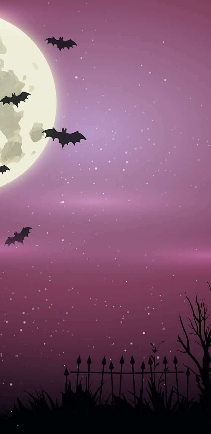 Minimalist Halloween 桌布 壁紙 — 蝙蝠在閃耀的滿月下翱翔，背景是繁星點點的紫色天空，下方是陰森的圍欄和光禿禿的樹木。