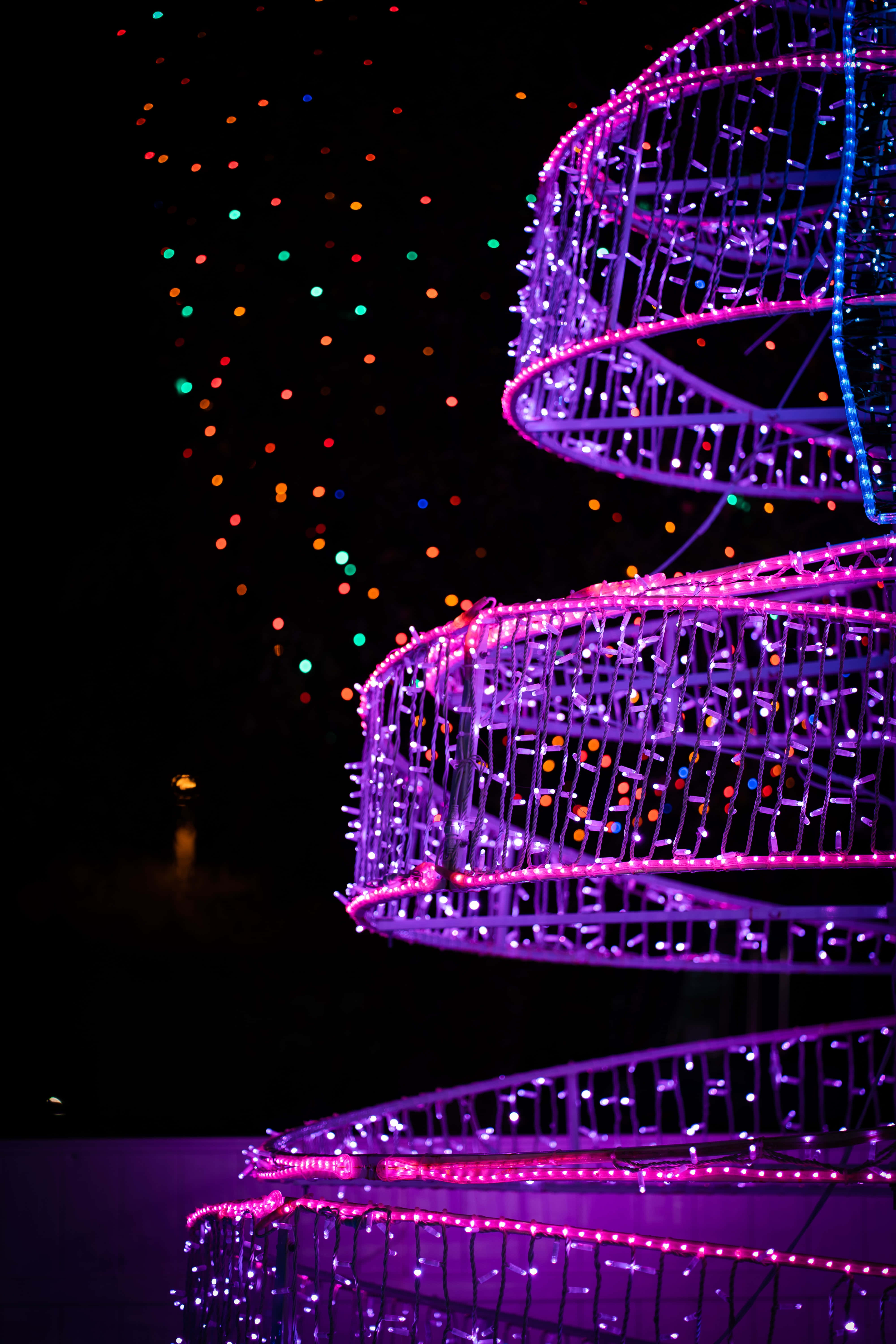Christmas Light 桌布 壁紙 — 螺旋形紫色燈光雕塑在點綴著彩色散景燈光的黑暗夜空中發光。