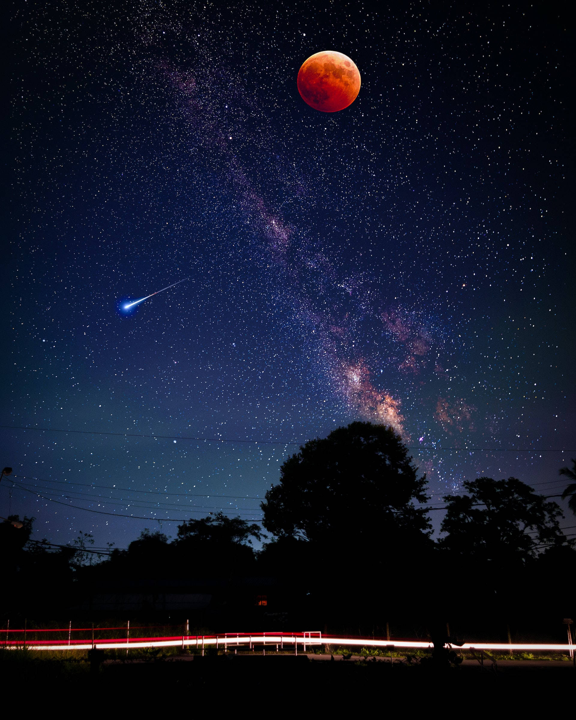 月光 桌布 壁紙 — 血月在繁星點點的夜空中發出紅色光芒，一顆明亮的流星劃過銀河，掠過剪影樹木和光跡。