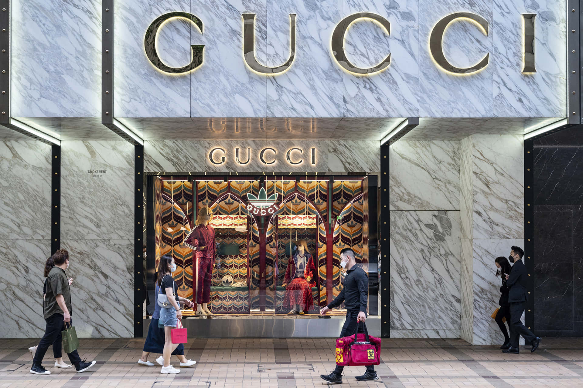 人們走過一間Gucci商店，有大理石牆壁和色彩繽紛的櫥窗展示。 — Gucci GIF 壁紙