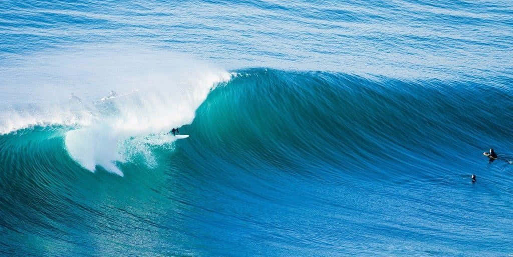 surfing 桌布 壁紙 — 衝浪者在明亮的日光下乘著巨大的藍綠色海浪，水花四濺。