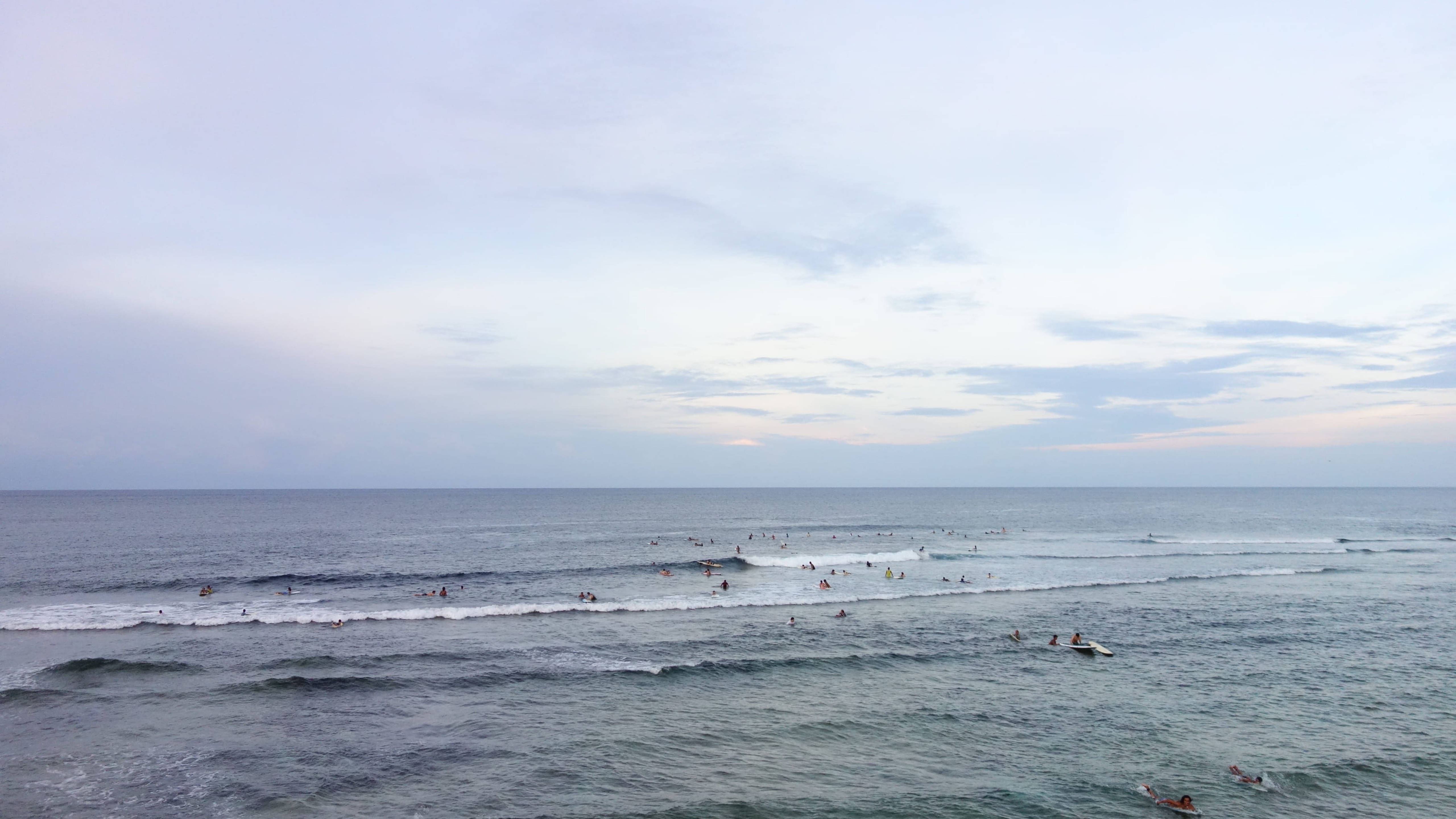 Siargao 桌布 壁紙 — 衝浪者在黎明時分柔和粉彩天空下駕馭溫柔的海浪。