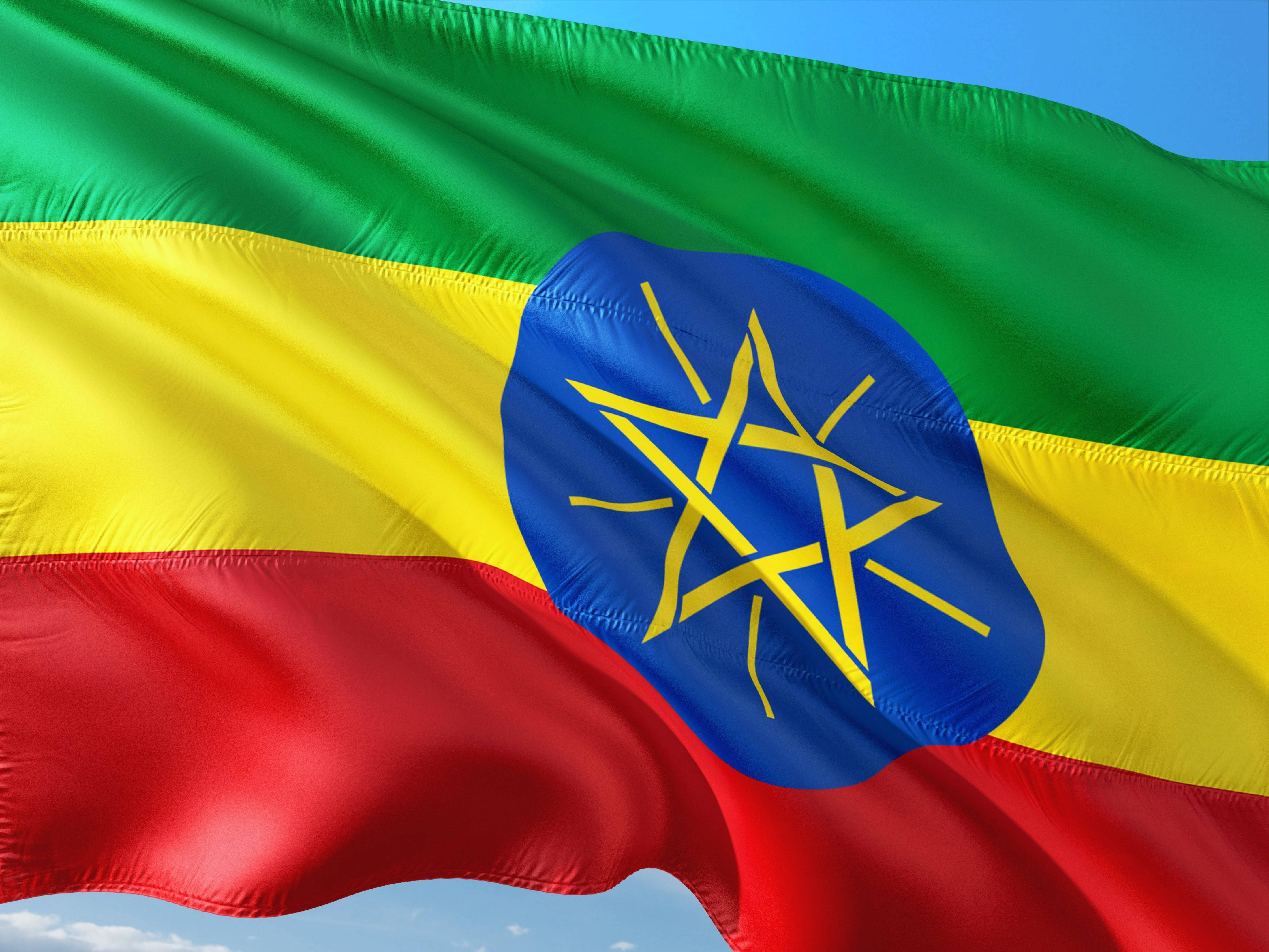 Ethiopia 桌布 壁紙 — 衣索比亞國旗在藍天白雲下動態飄揚，綠色、黃色和紅色的條紋以及中央的藍色星星標誌細節清晰。