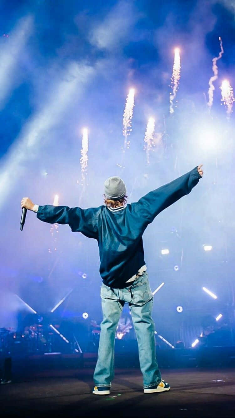 Justin Bieber 2021 桌布 壁紙 — 表演者在舞台上張開雙臂，藍色舞台燈光下煙火在上方爆炸。