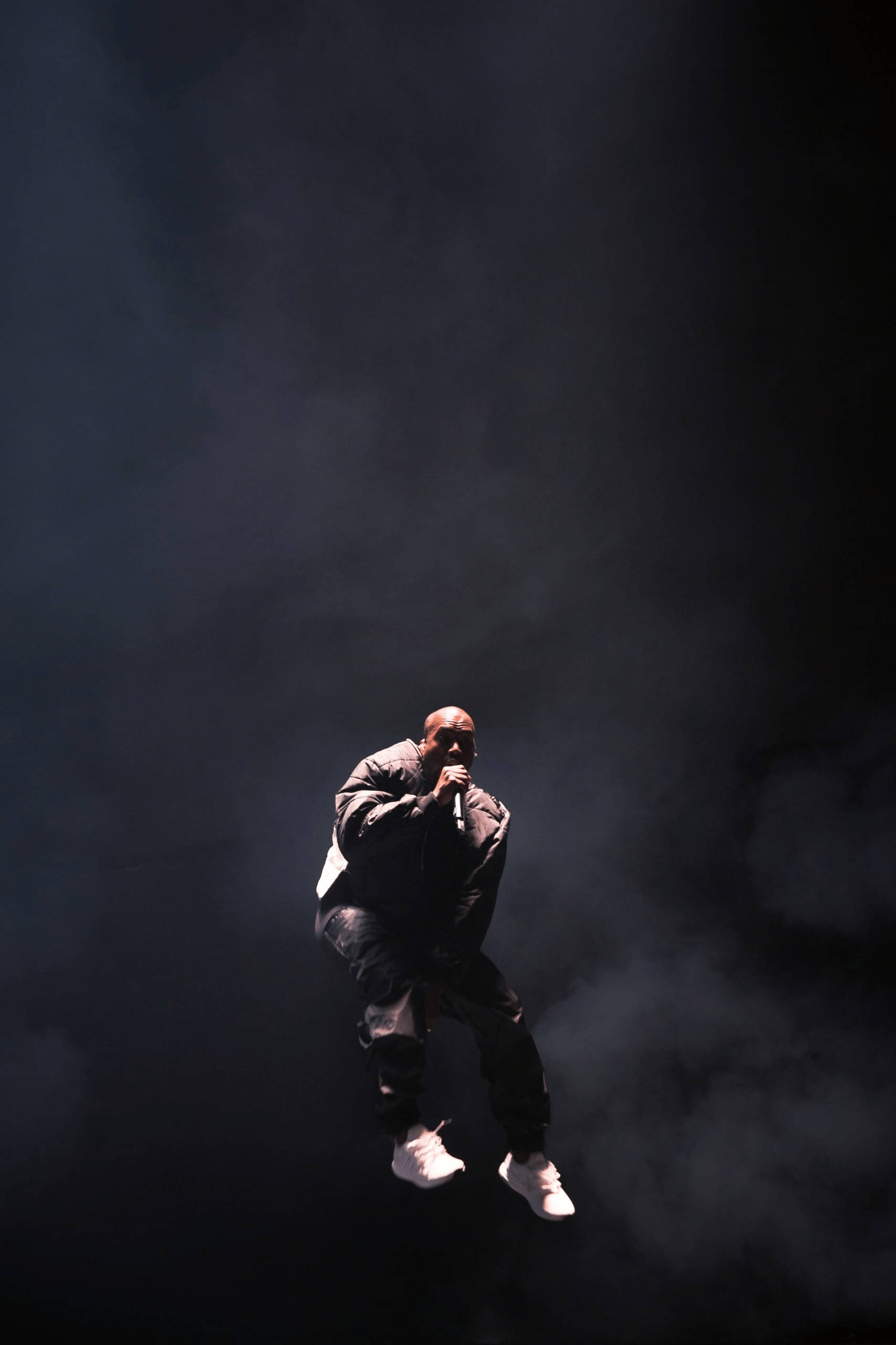 Kanye 桌布 壁紙 — 表演者在黑暗煙霧中懸浮在半空，在戲劇性的舞台燈光下握著麥克風。