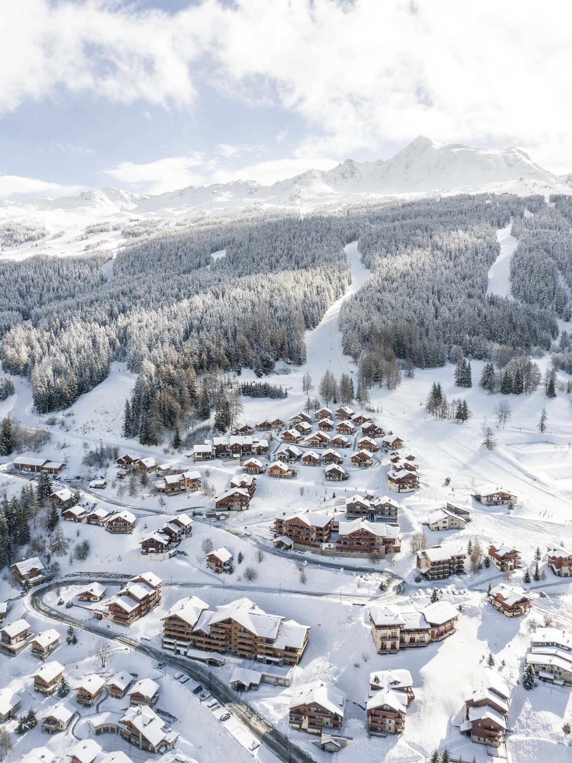 Ski Resort 桌布 壁紙 — 被常綠森林環繞的積雪山村的鳥瞰圖，滑雪道蜿蜒穿過山峰。