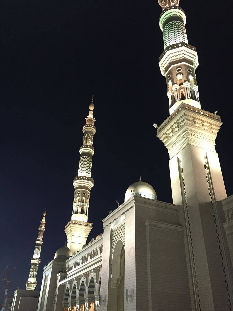 Madina 桌布 壁紙 — 被照亮的清真寺宣禮塔和圓頂在深邃的夜空中雄偉地聳立，溫暖的金色燈光突顯了複雜的建築細節。