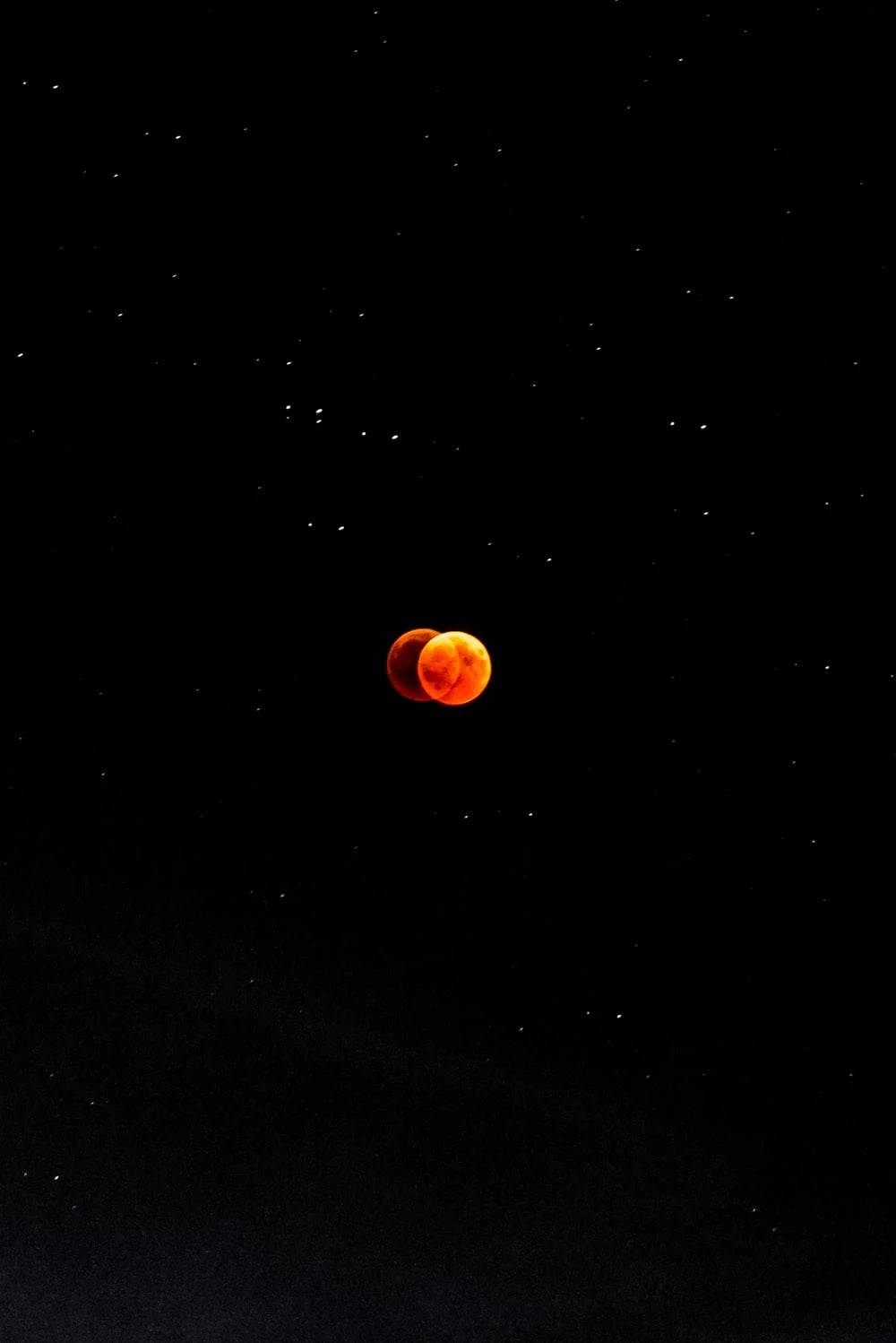 Eclipse 桌布 壁紙 — 被陰影遮蔽的血月，在繁星點點的夜空中發出火橙色光芒。