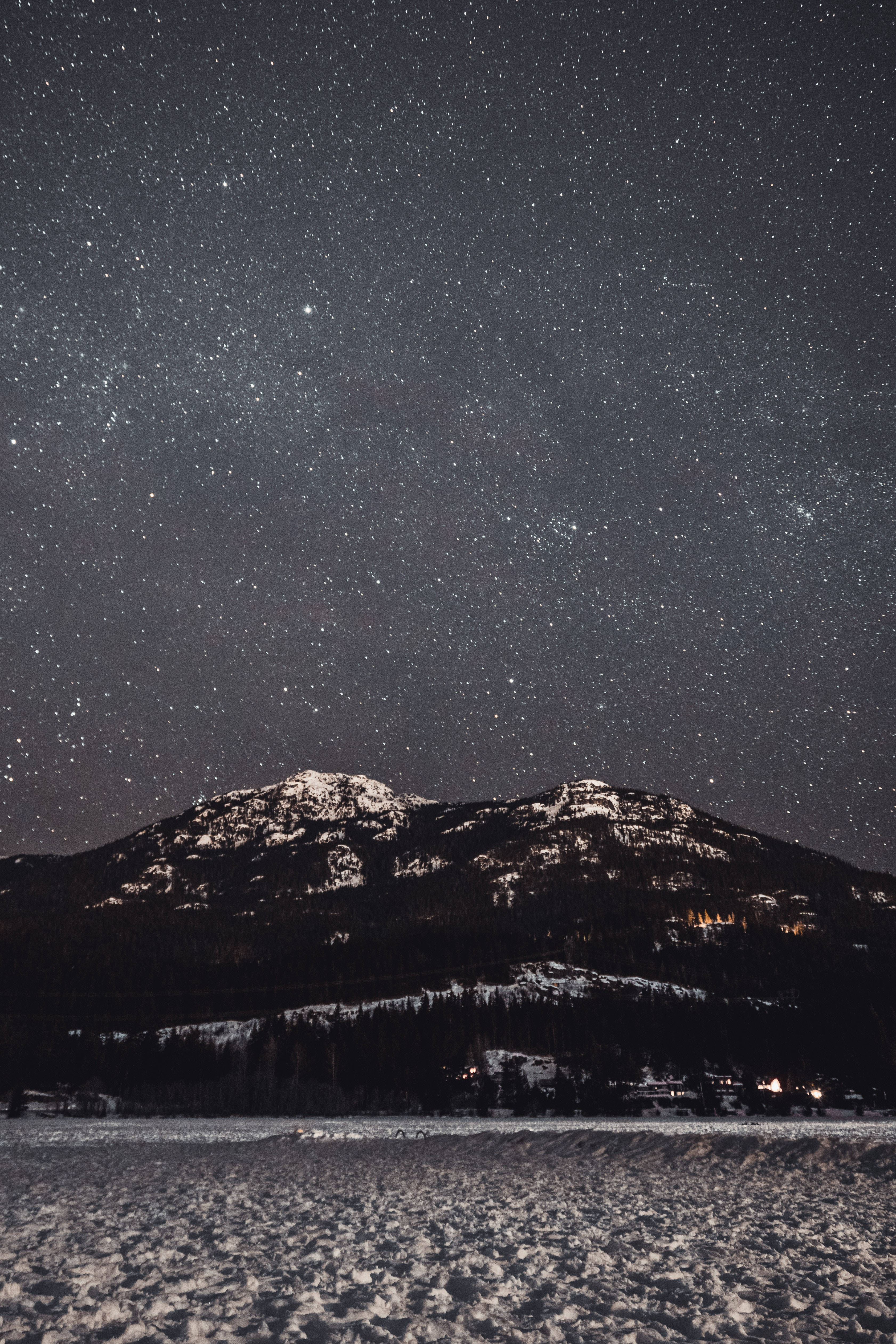 iPhone 7 plus space 桌布 壁紙 — 被雪覆蓋的山脈，在密集的星空下，下方遠處村莊散落著燈光。