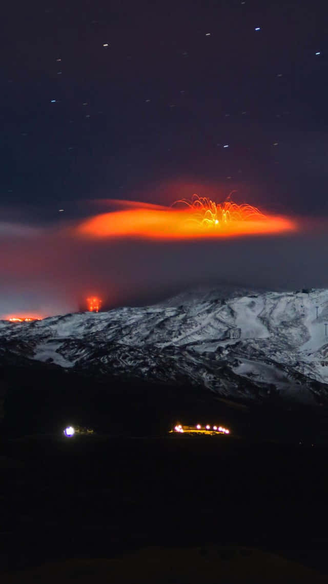 夜空 桌布 壁紙 — 被雪覆蓋的山脈在夜間爆發，熾熱的橙色熔岩照亮了星空。