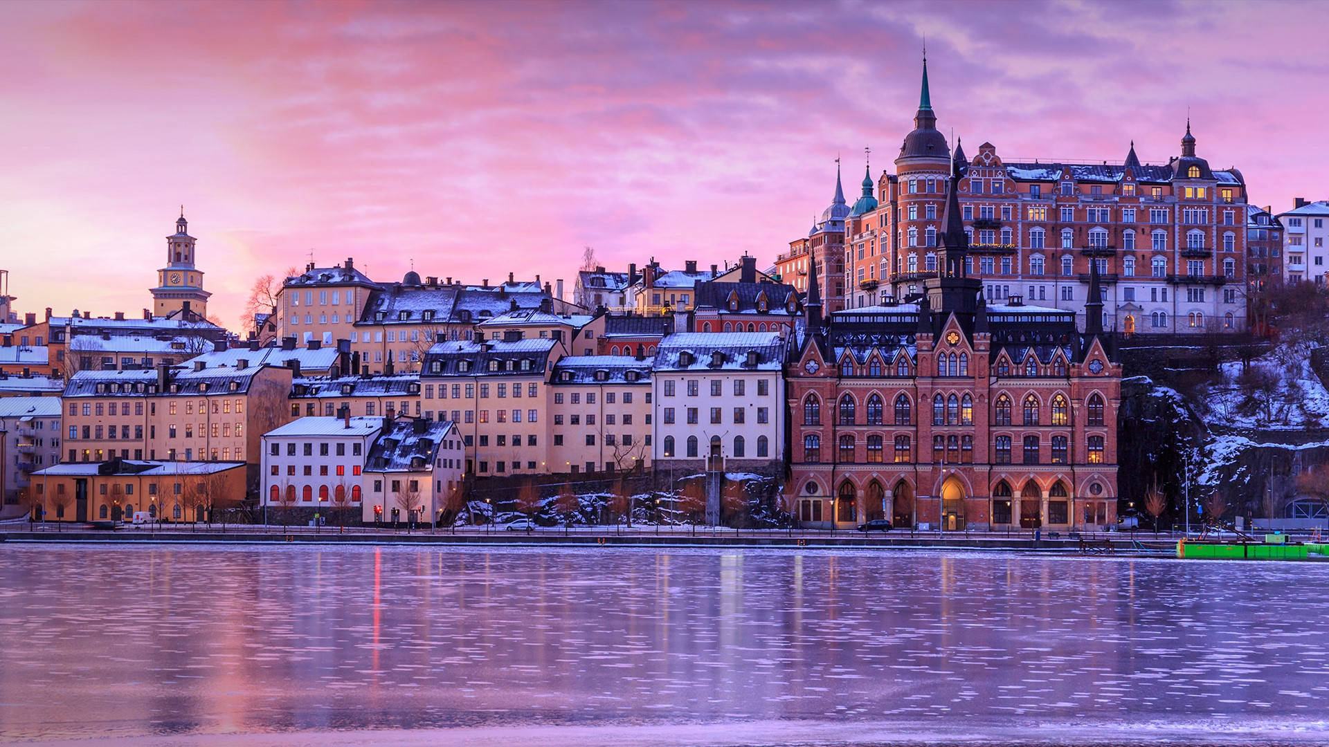 Sweden 桌布 壁紙 — 被雪覆蓋的歷史建築在冰封的河面上反射出充滿活力的粉紅色和紫色日落天空，溫暖地發光。