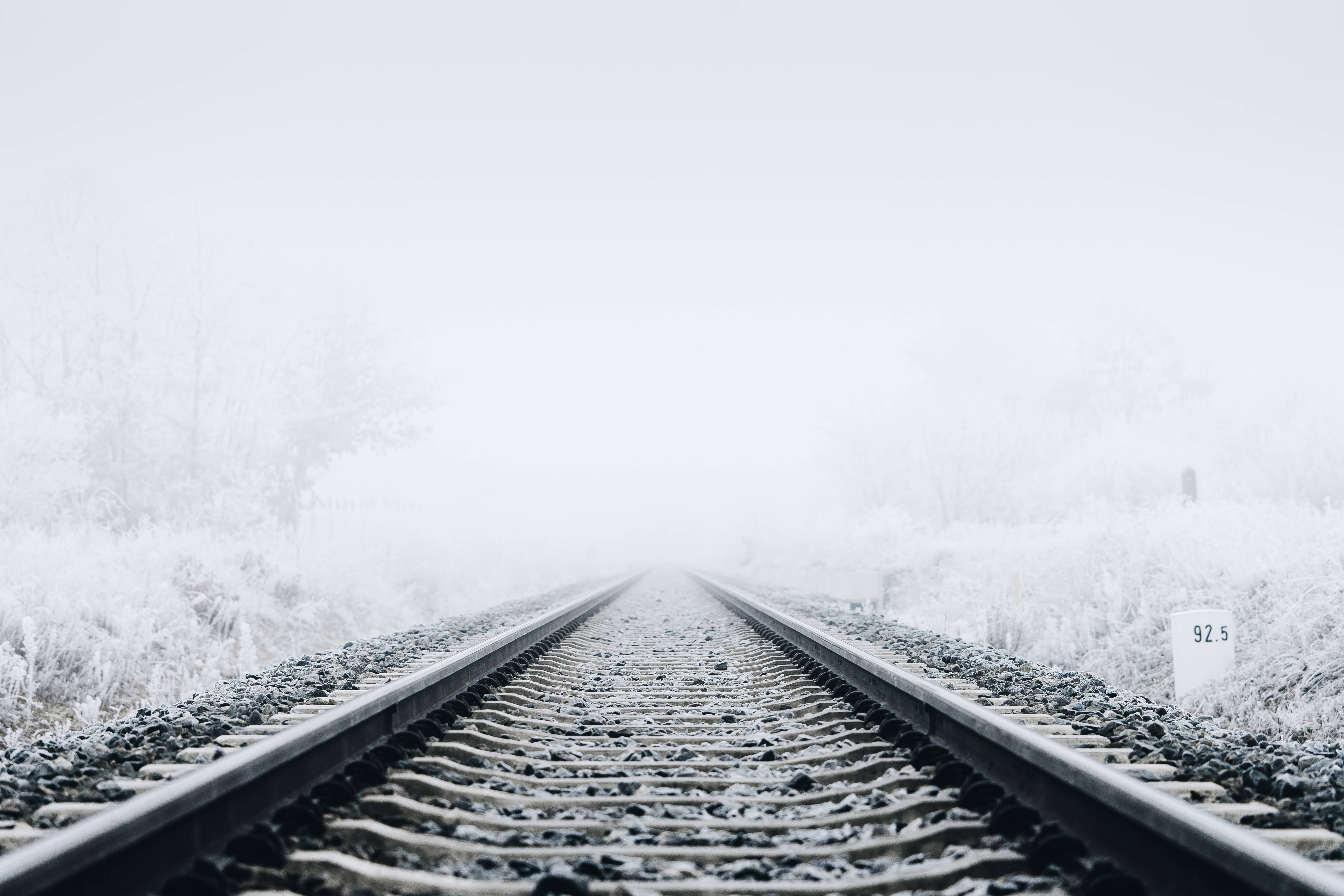 冬季桌面 桌布 壁紙 — 被雪覆蓋的鐵路軌道延伸進一個霧濛濛的白色冬季景觀，兩旁是結霜的樹木。