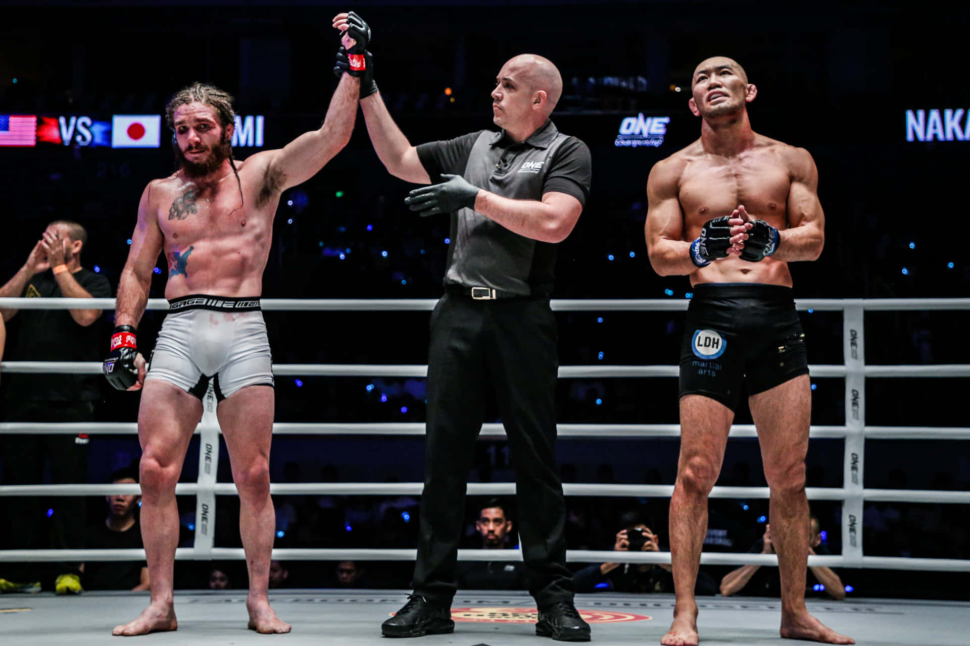 UFC 桌布 壁紙 — 裁判在燈光明亮的MMA八角籠中舉起勝者的手臂，而失敗的拳手站在他旁邊。