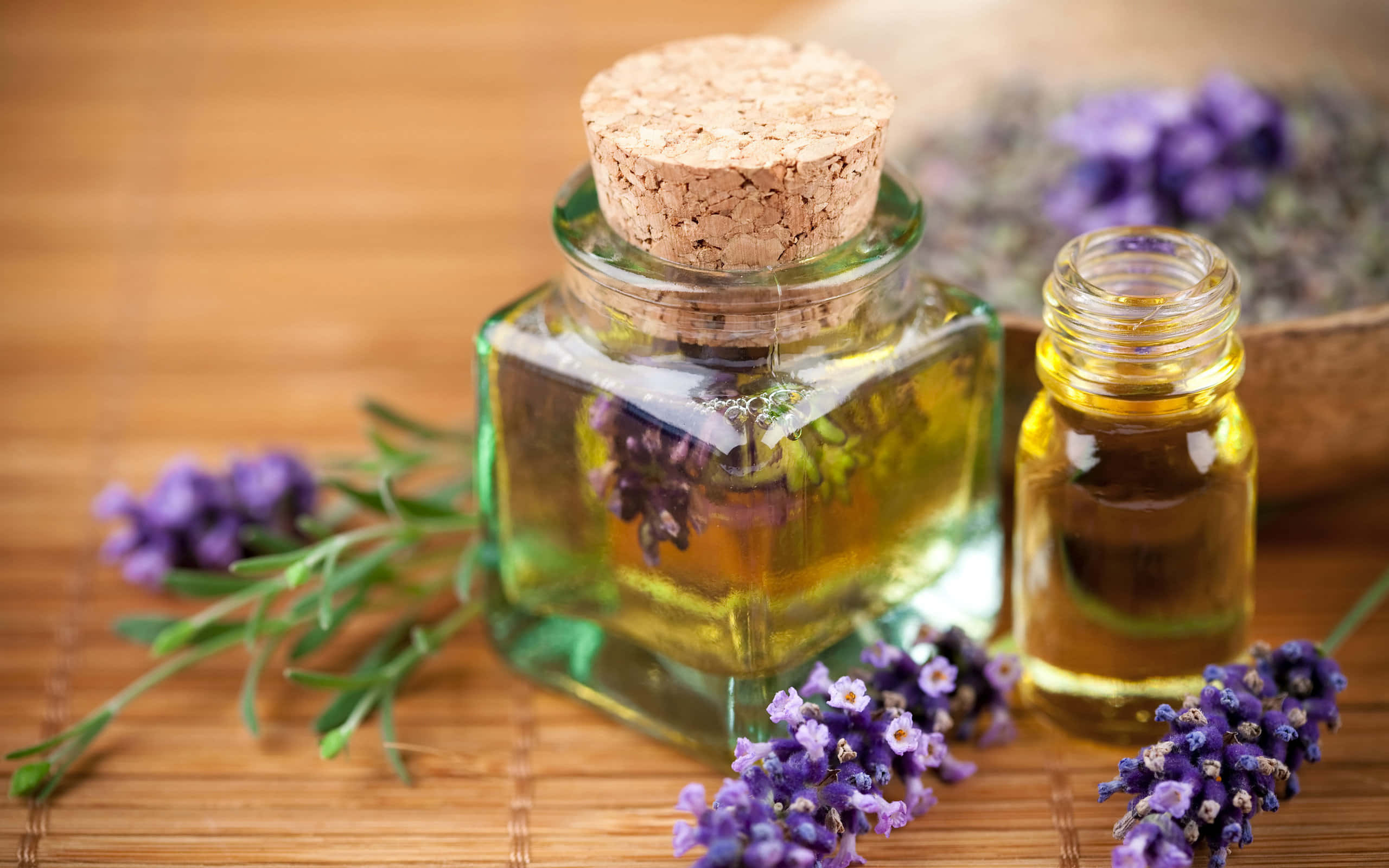 Essential Oil 桌布 壁紙 — 裝滿金色薰衣草油的玻璃瓶放在竹蓆上，旁邊有新鮮的紫色薰衣草枝。