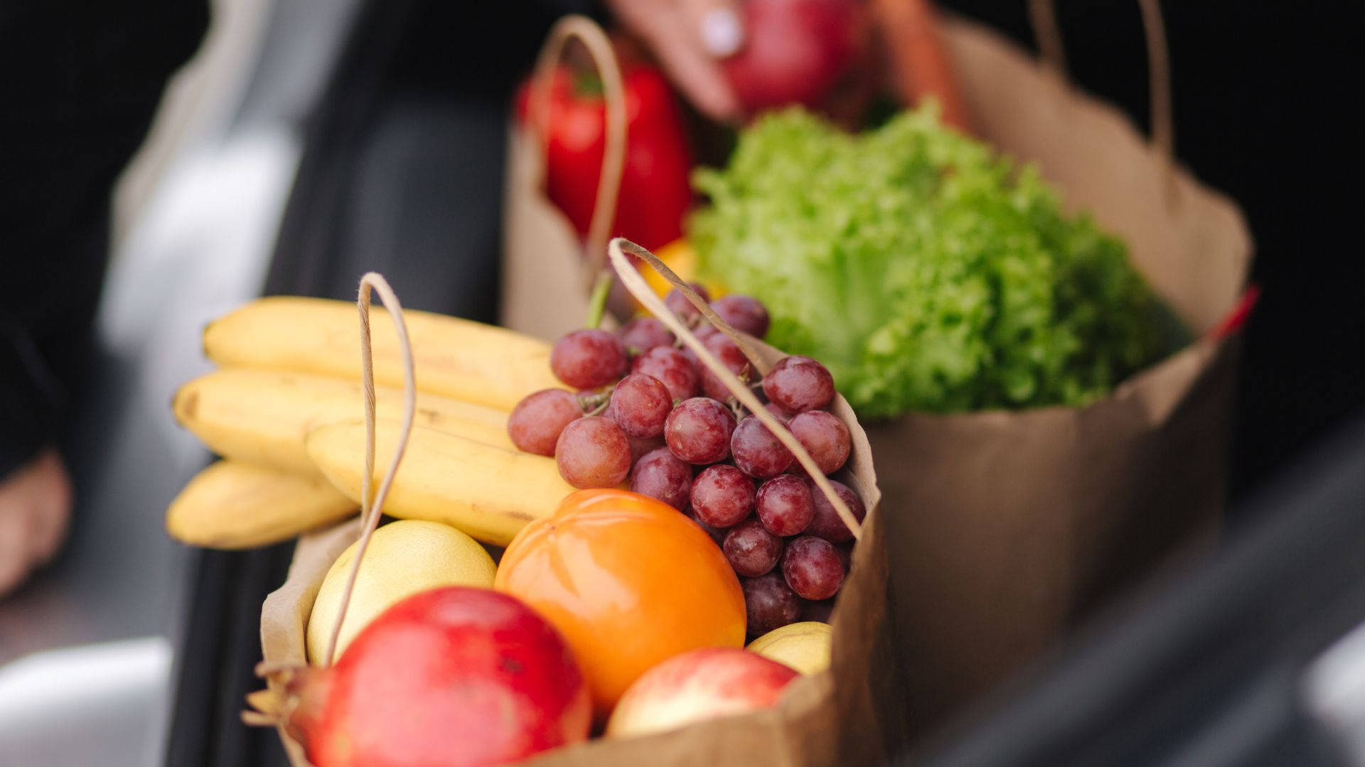 Fruits And Vegetables 桌布 壁紙 — 裝滿香蕉、葡萄、柳橙和生菜的新鮮農產品袋放在汽車後車廂，準備製作健康餐點。