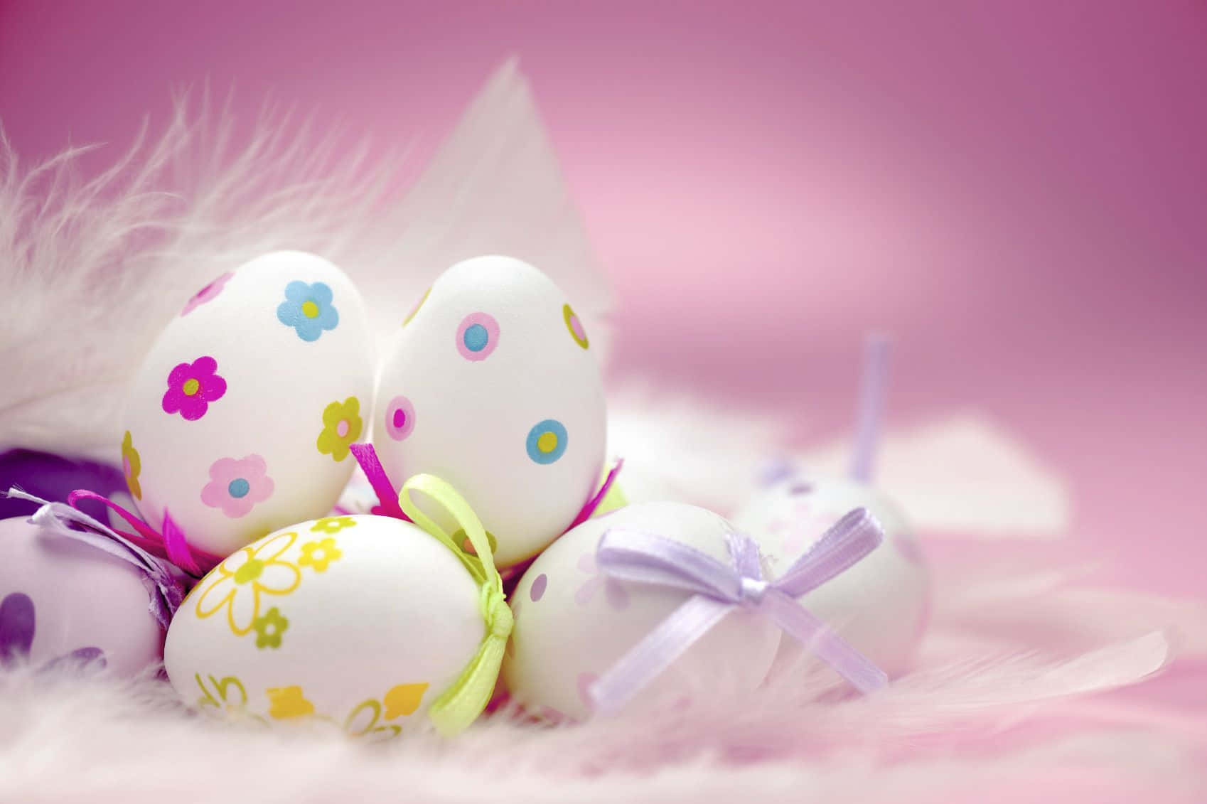 Cute Happy Easter 桌布 壁紙 — 裝飾有花卉圖案和絲帶的復活節彩蛋，放置在柔軟的白色羽毛上，背景是夢幻的粉紅色。