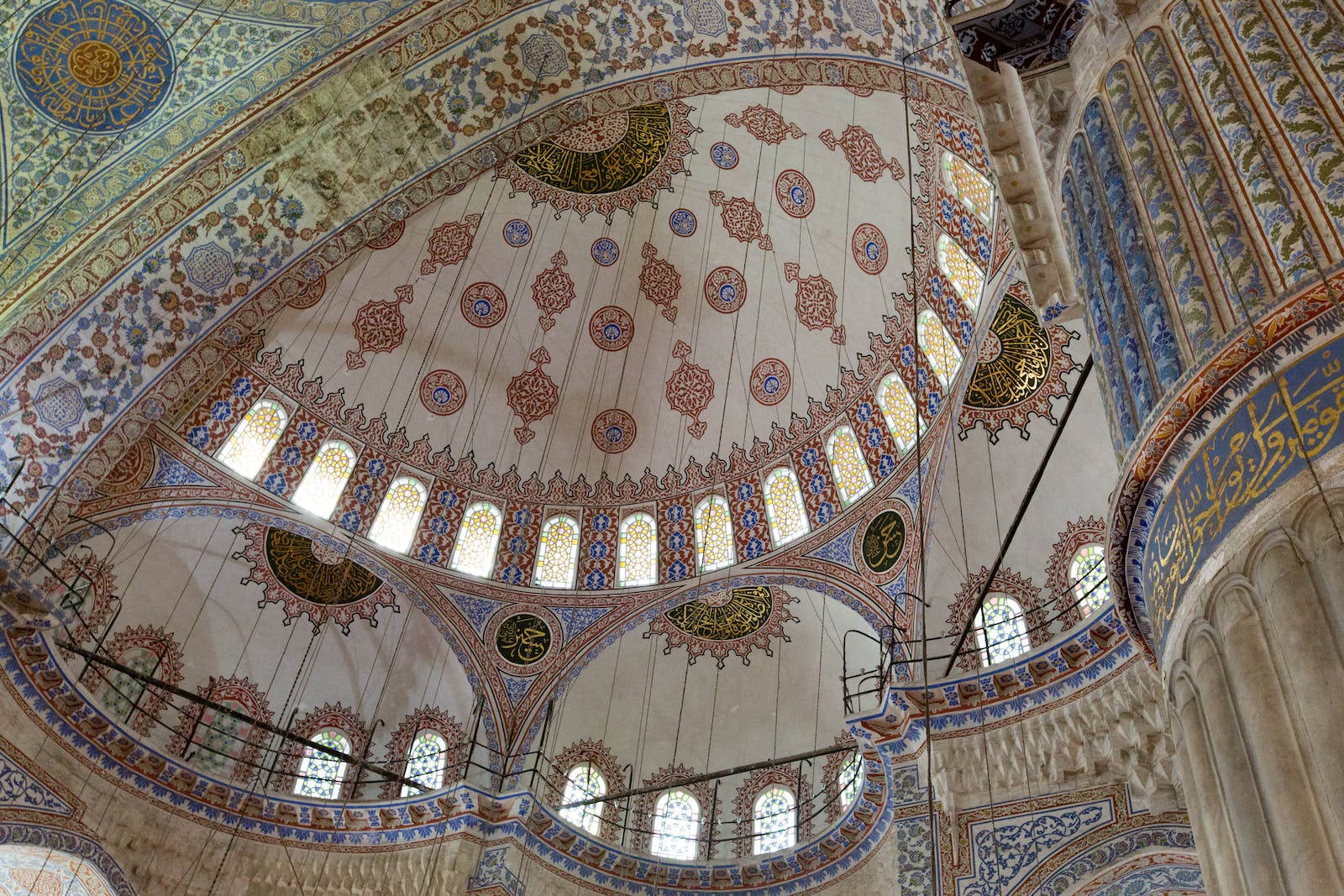 HD Islamic 桌布 壁紙 — 裝飾華麗的圓頂內部，帶有精緻的藍色、金色和紅色瓷磚工藝，以及拱形窗戶，讓柔和光線透入。