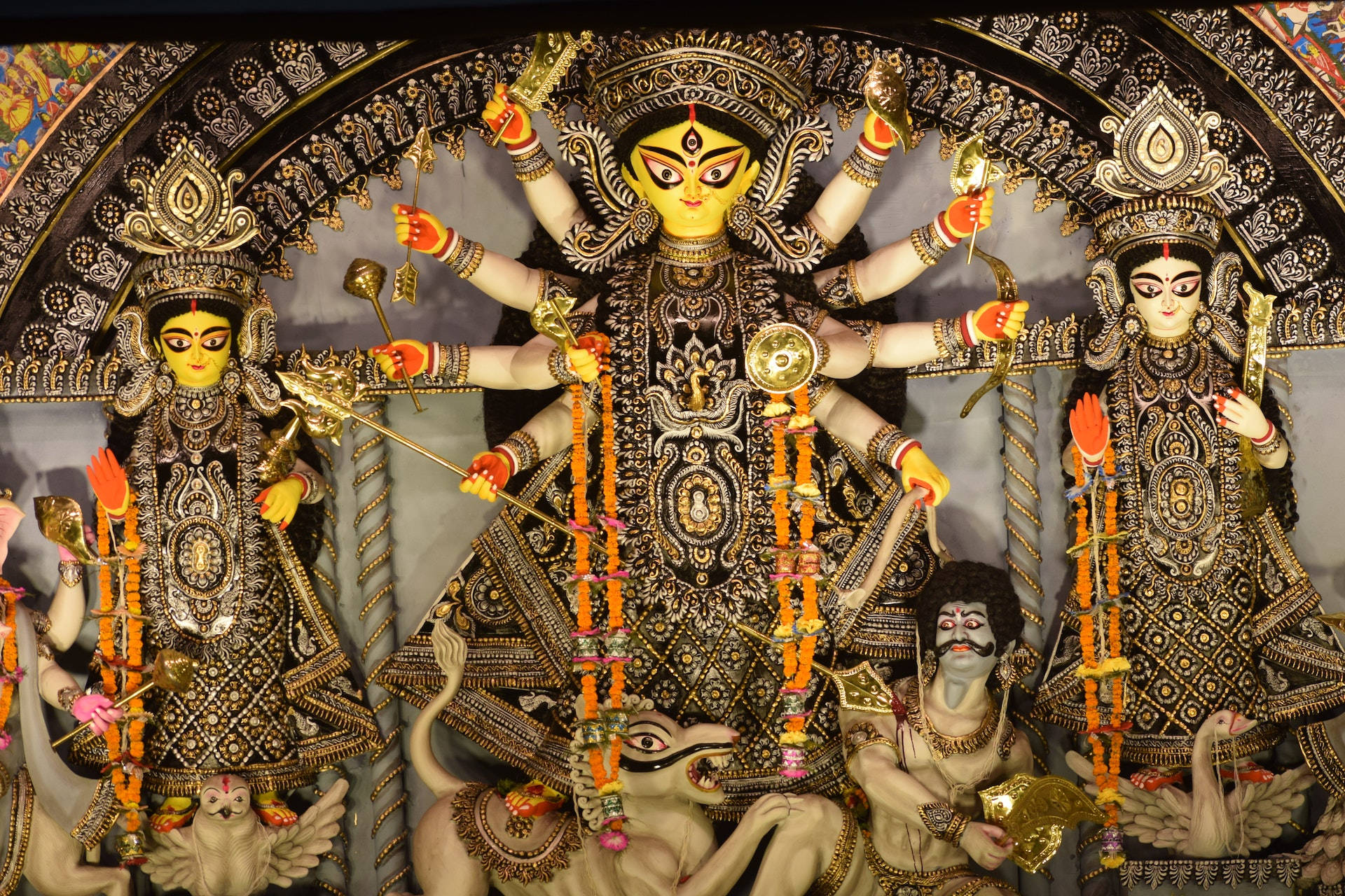 Durga 桌布 壁紙 — 裝飾華麗的杜爾迦普迦神像，有多隻手臂和武器，矗立在華麗的拱門下，周圍有侍從和供品。