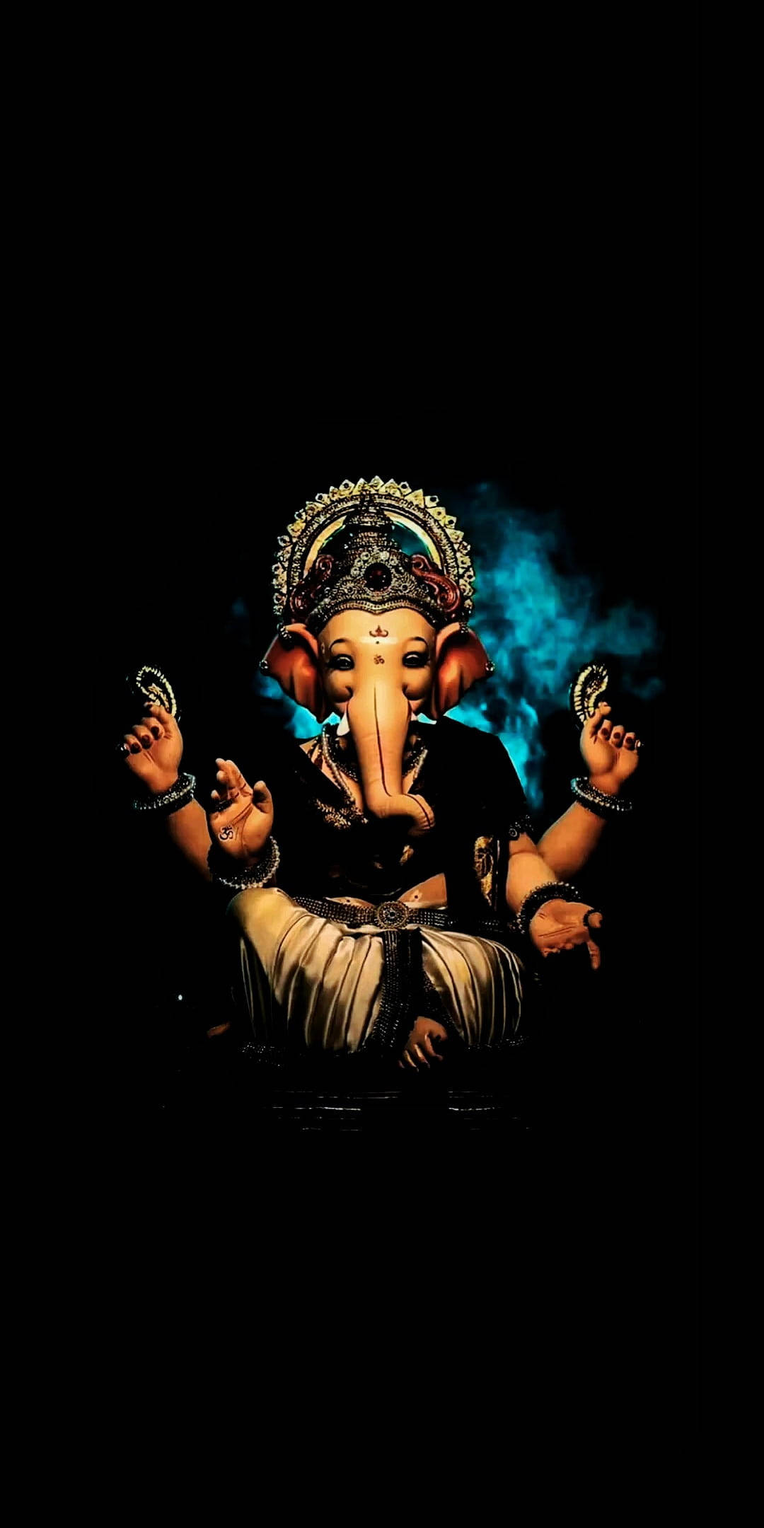 Ganesh 桌布 壁紙 — 裝飾華麗的皇冠和珠寶的象頭神雕像，在黑暗背景後方有發光的藍色煙霧，靜靜地坐著。