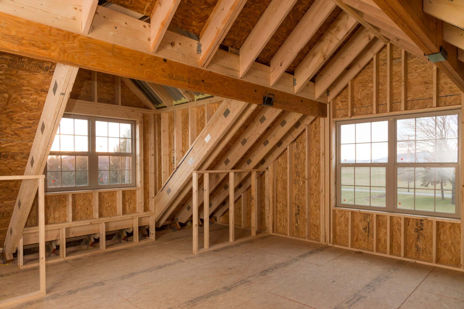 cabin 桌布 壁紙 — 裸露的木樑和OSB牆壁框出一個正在施工的明亮閣樓，大窗戶俯瞰著一片草地。