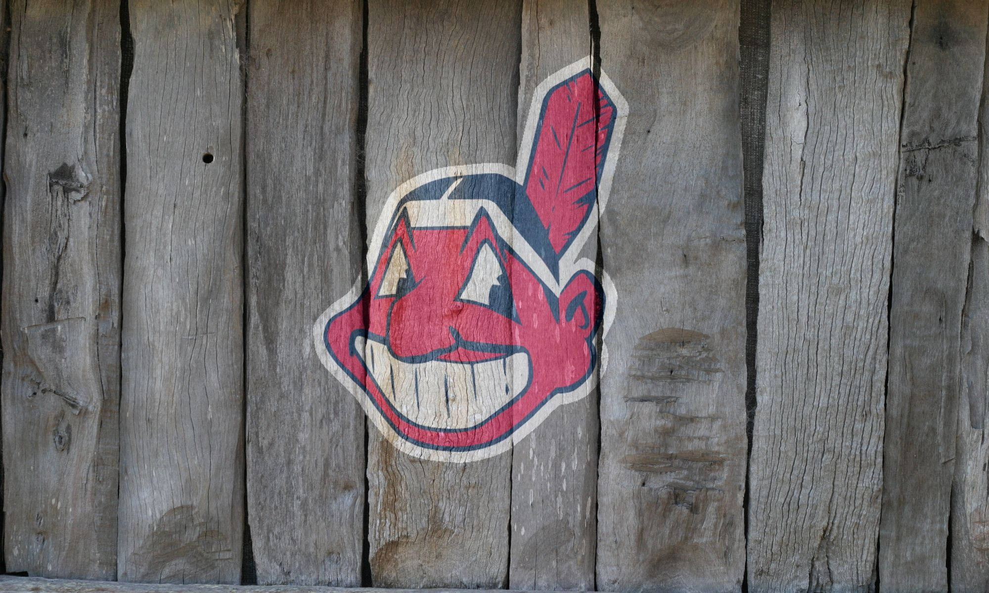 Cleveland Indians 桌布 壁紙 — 褪色的紅、藍、白 Chief Wahoo 標誌，繪在風化的灰色木板上。