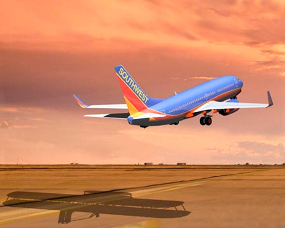 Southwest 桌布 壁紙 — 西南航空飛機在日落時分起飛，在溫暖的橙色天空下在跑道上投下長長的影子。