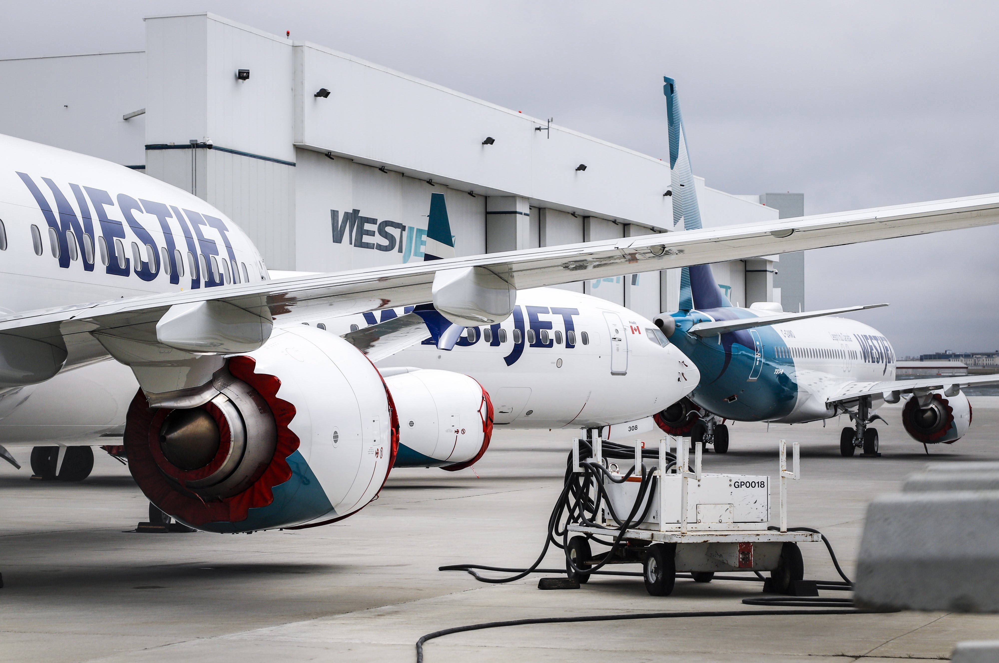 飛機 桌布 壁紙 — 西捷航空飛機停泊在機場閘口，配備登機橋和地勤服務設備，天空多雲。