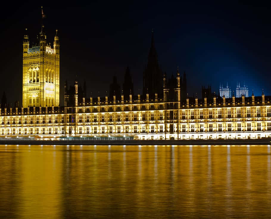 House Of Parliament 桌布 壁紙 — 西敏宮在夜晚溫暖地發光，其複雜的哥德式建築完美地倒映在泰晤士河平靜的水面上。